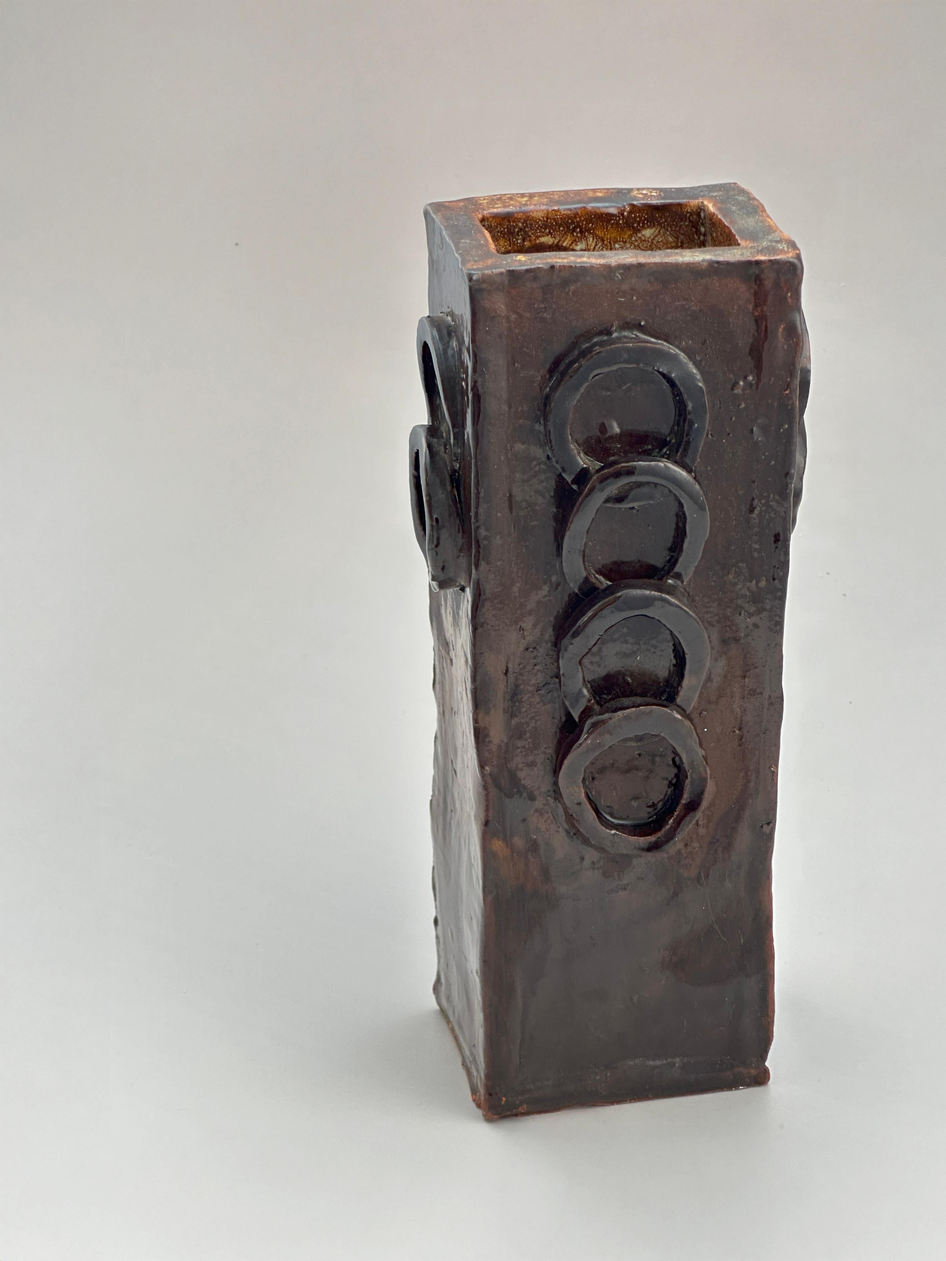 Eine brutalistische Studio-Töpfervase, handgefertigt aus Terrakotta, aus den 1970er Jahren, Vereinigtes Königreich.

Die rechteckige Vase ist mit applizierten kreisförmigen Ringen verziert, die sich entlang der Oberfläche schichtweise anordnen und
