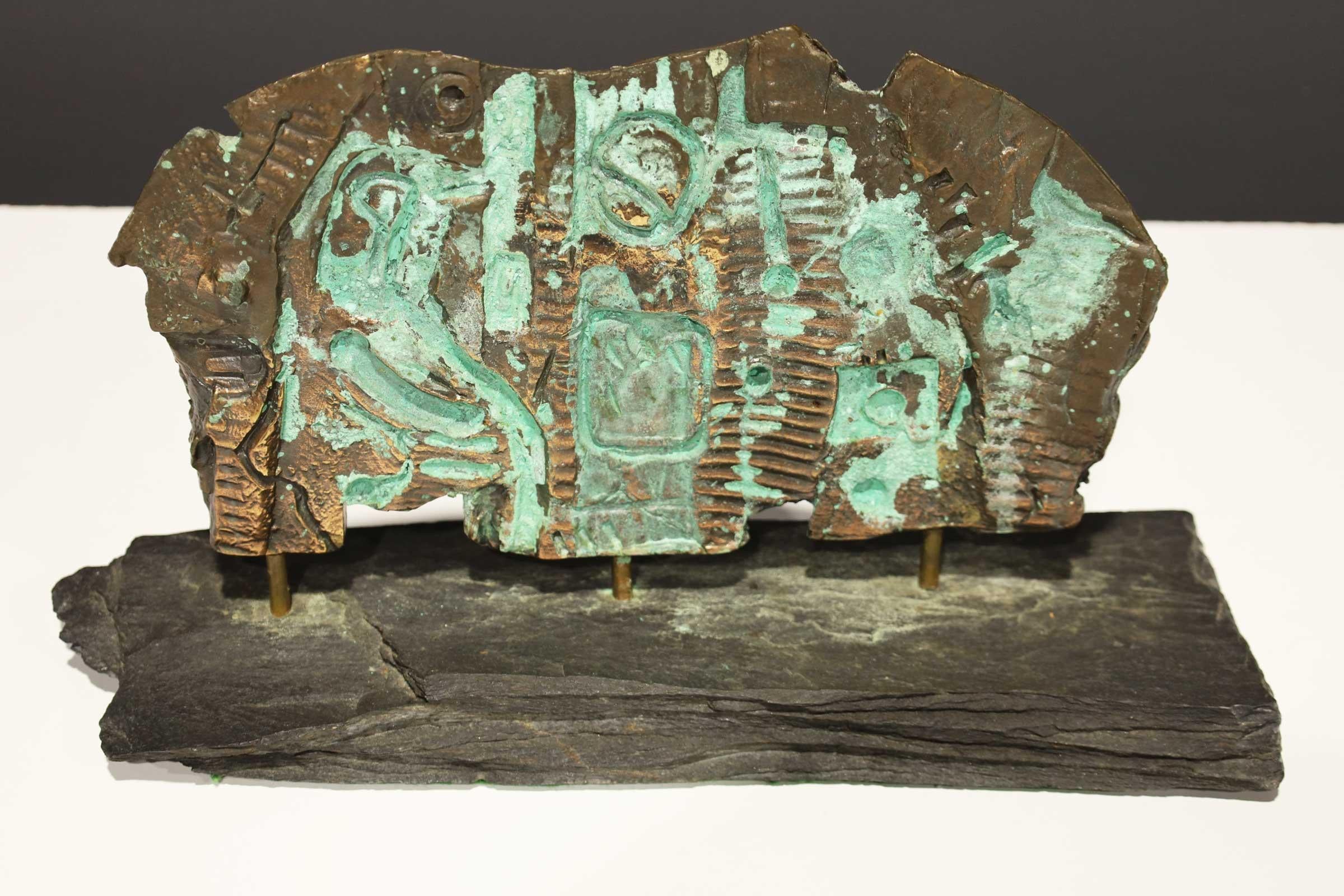 Bronze bien oxydé, en forme de dalle, avec un décor figuratif imprimé, reposant sur une base sédimentaire. D'une importante succession.