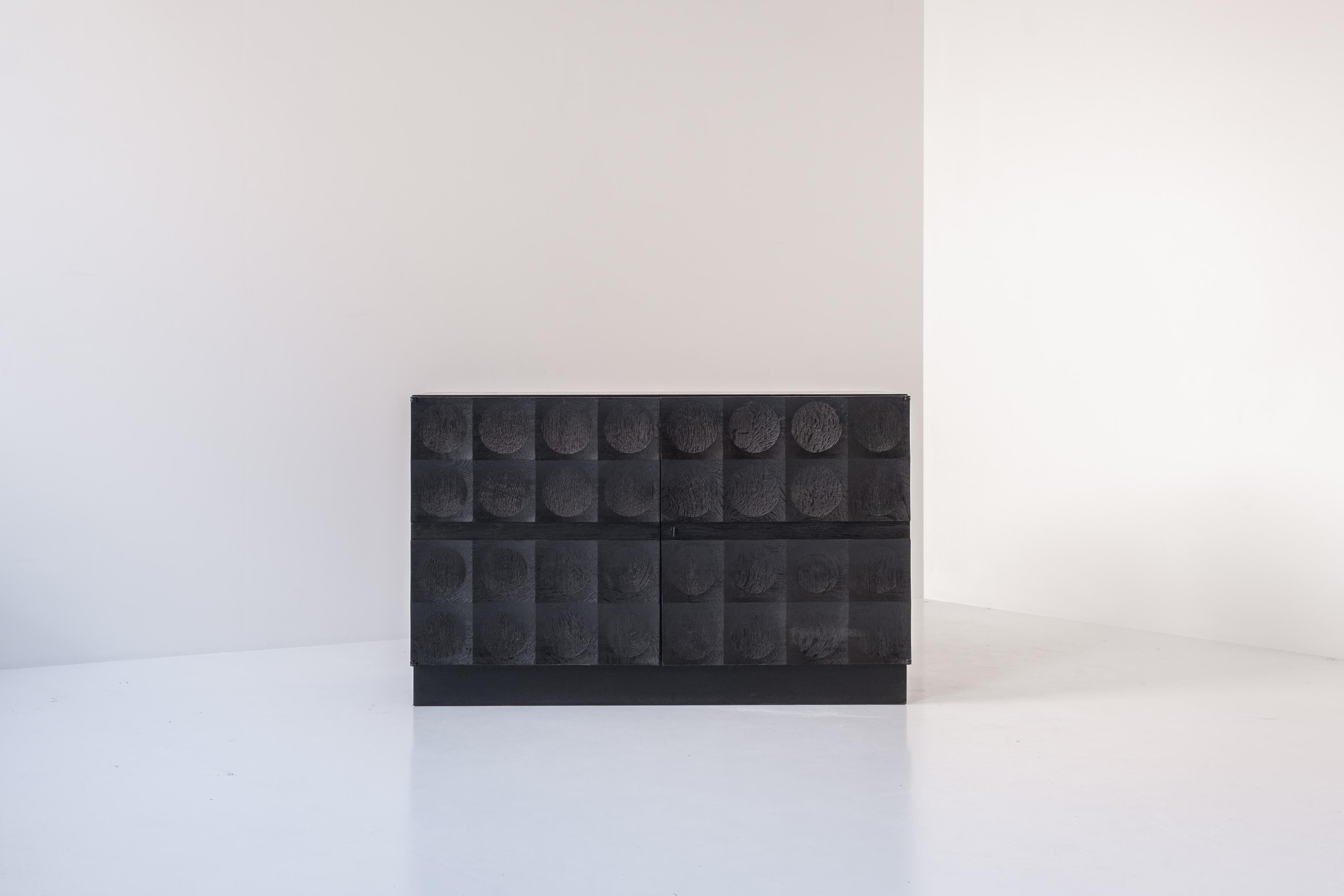 Armoire brutaliste en chêne teinté noir par J. Batenburg For MI, Belgique vers 1969. Ce meuble étonnant présente une série de motifs sculptés répétitifs, qui confèrent au buffet une apparence solide. Les deux portes couvrent un espace bar à gauche