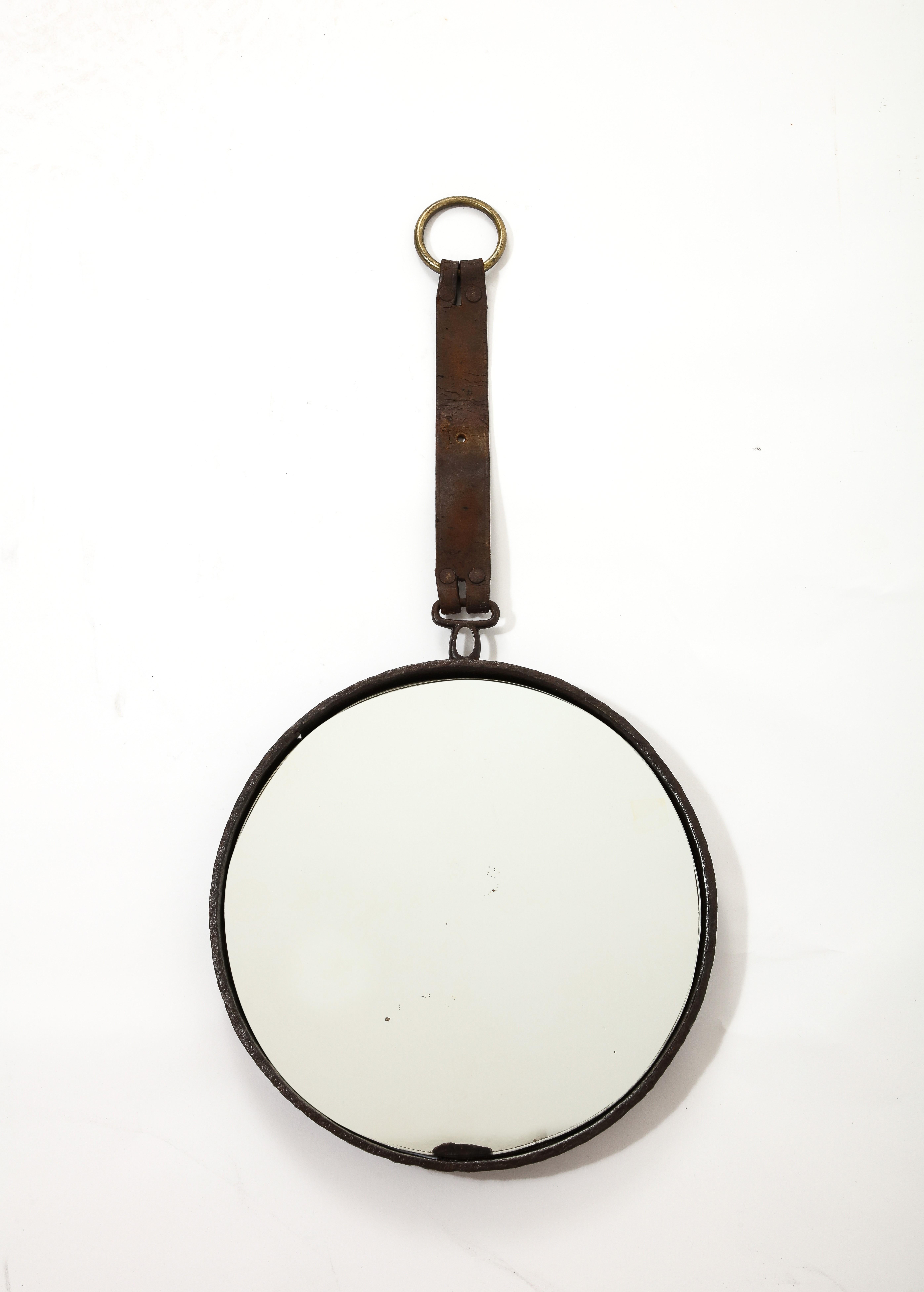 Brutalist cast iron mirror with a deep brown leather strap and a brass finishing ring. In fair vintage condition. Markings and wear on leather strap. Oxydation on the mirror especially in one specific area close to the rim.
 