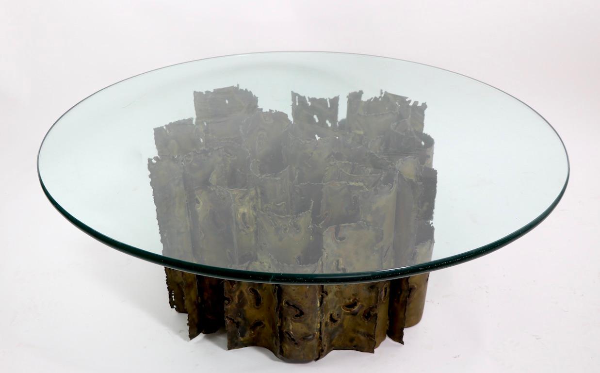 Impressive brutalist cathedral coffee table by Silas Seandel, circa 1970s. The table features a thick (.75 in.) round plate glass top (shows inconsequential cosmetic scratches) which rests on an incredible sculptural torch cut brass/bronze base.