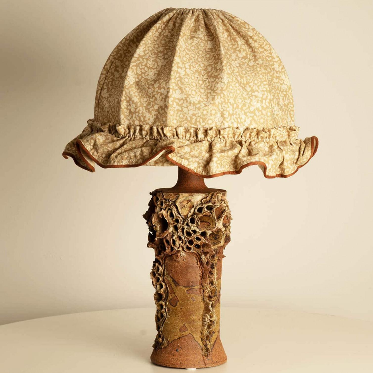 The ceramic base of this Bodil Marie Nielsen lamp exemplifies the Danish Brutalist style of the 1960s, characterized by its raw, tactile forms and organic textures. Crafted from stoneware, the base has matte and glossy finishes, achieved through a