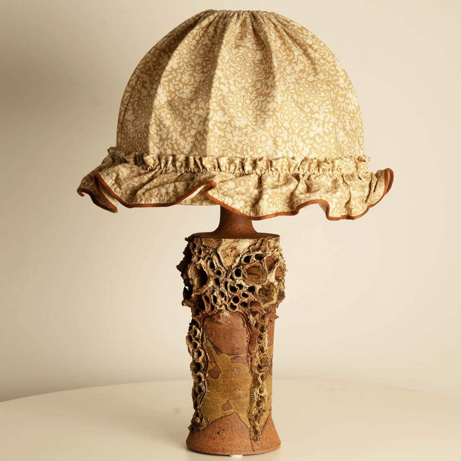 The ceramic base of this Bodil Marie Nielsen lamp exemplifies the Danish Brutalist style of the 1960s, characterized by its raw, tactile forms and organic textures. Crafted from stoneware, the base has matte and glossy finishes, achieved through a