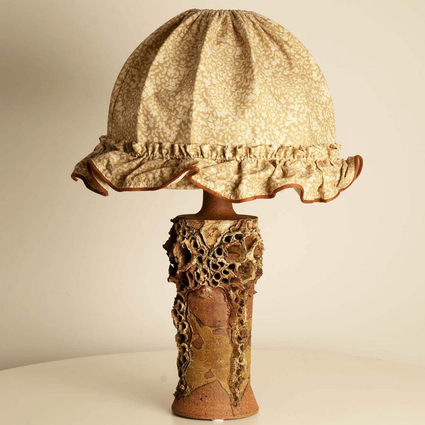 The ceramic base of this Bodil Marie Nielsen lamp exemplifies the Danish Brutalist style of the 1960s, characterized by its raw, tactile forms and organic textures. Crafted from stoneware, the base has matte and glossy finishes, achieved through a