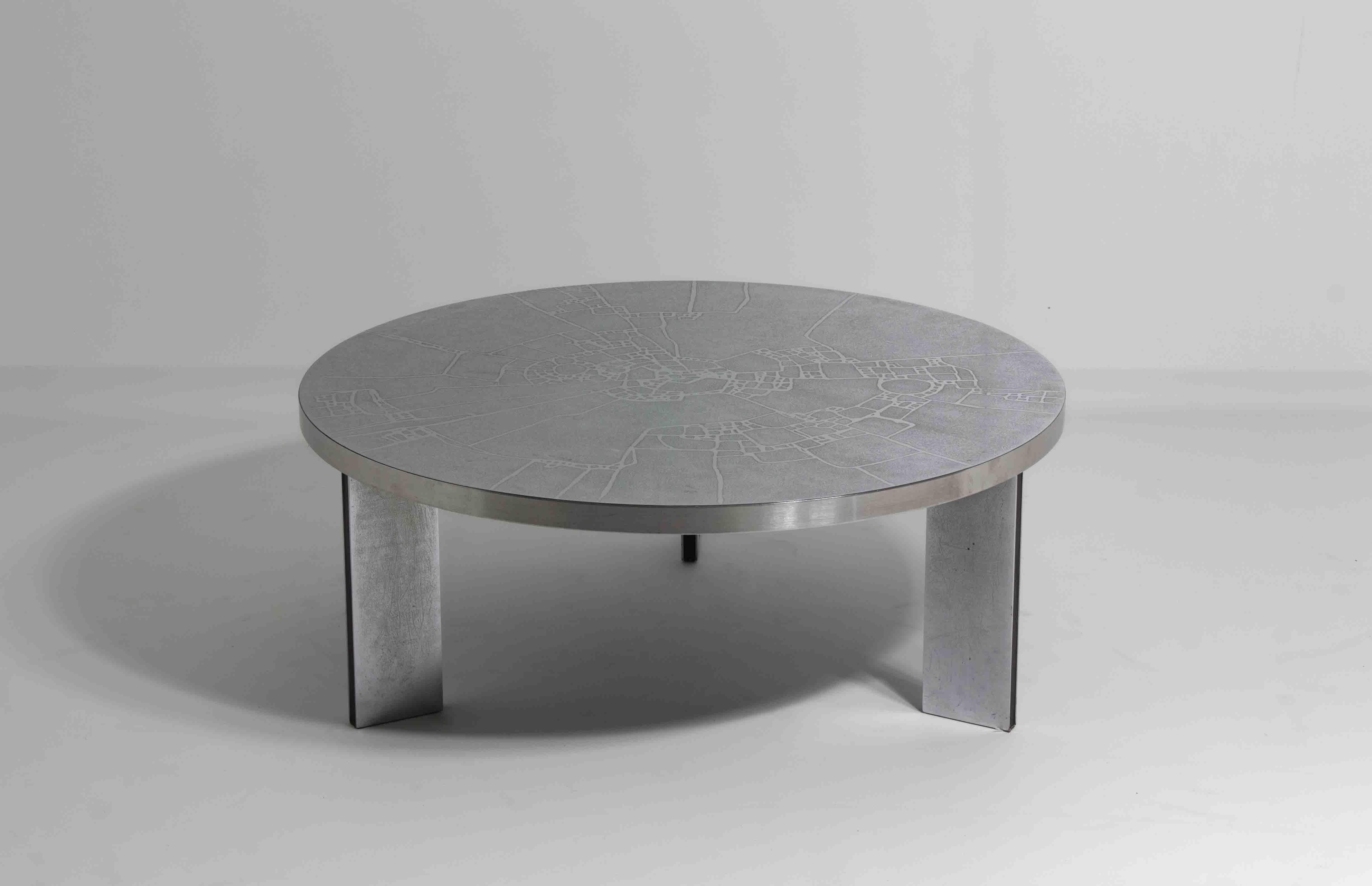 This round coffee table was designed by Heinz Lilienthal in the 1960s. The top is finished in etched chrome with a detailed pattern. It has a slightly textured surface with smooth, raised lines. The edge is framed in brushed metal, giving it a clean