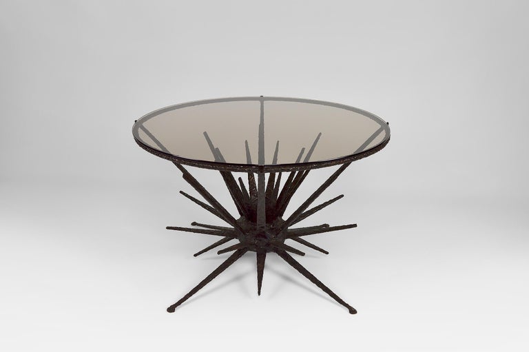 Elegant round coffee / side / pedestal table composed of a wrought iron structure in the shape of spades, sea urchin or star type ; and its circular smoked glass top.

The metal has a nice grainy / textured finish.
Very qualitative work.

Brutalist