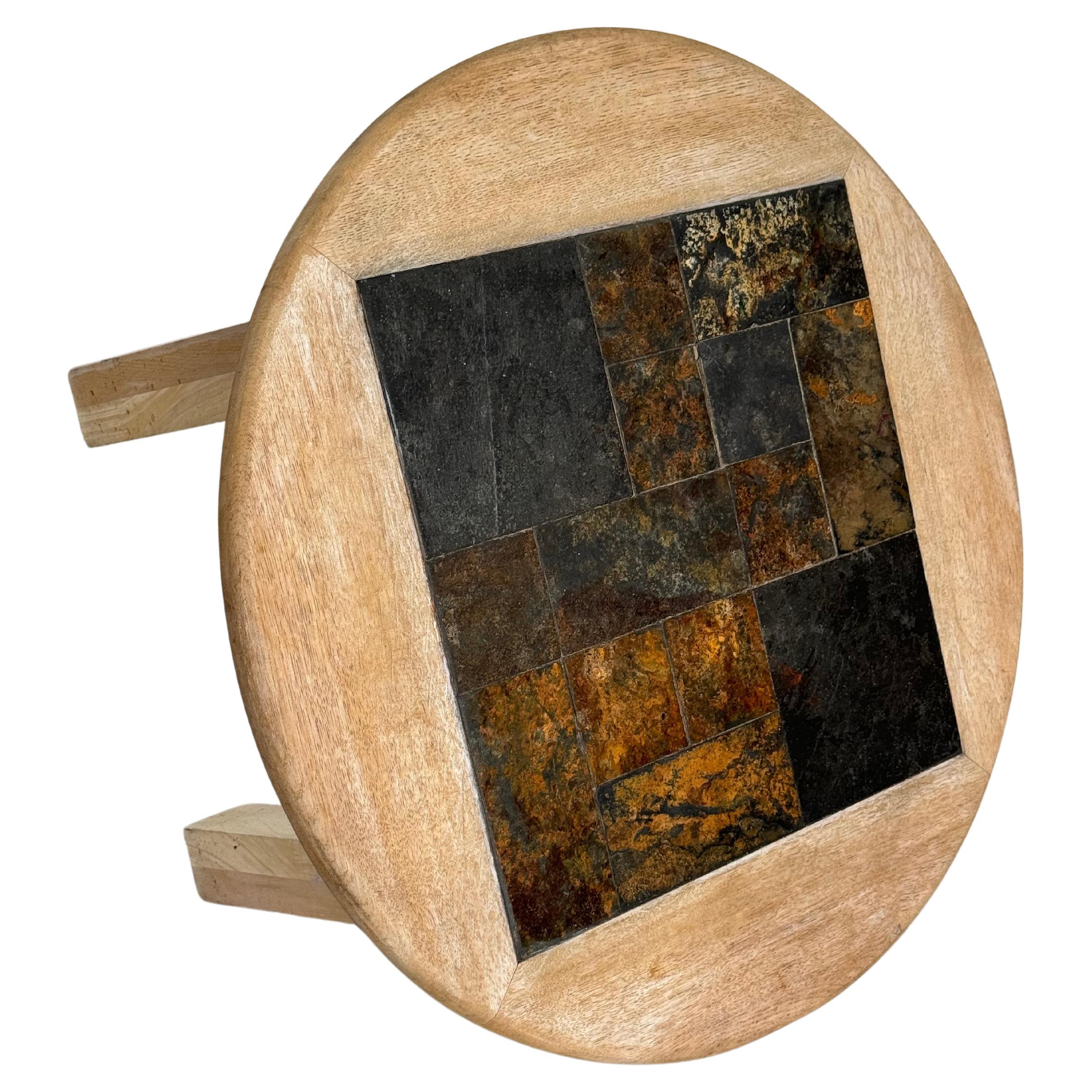 Belle table basse au design brutaliste.

Structure en bois brut (décapé), plateau circulaire incrusté d'une plaque de pierre d'ardoise, assemblée en mosaïque pour former un carré.

Hauteur du plateau : 42 cm
Épaisseur du plateau : 3 cm
Diamètre : 73