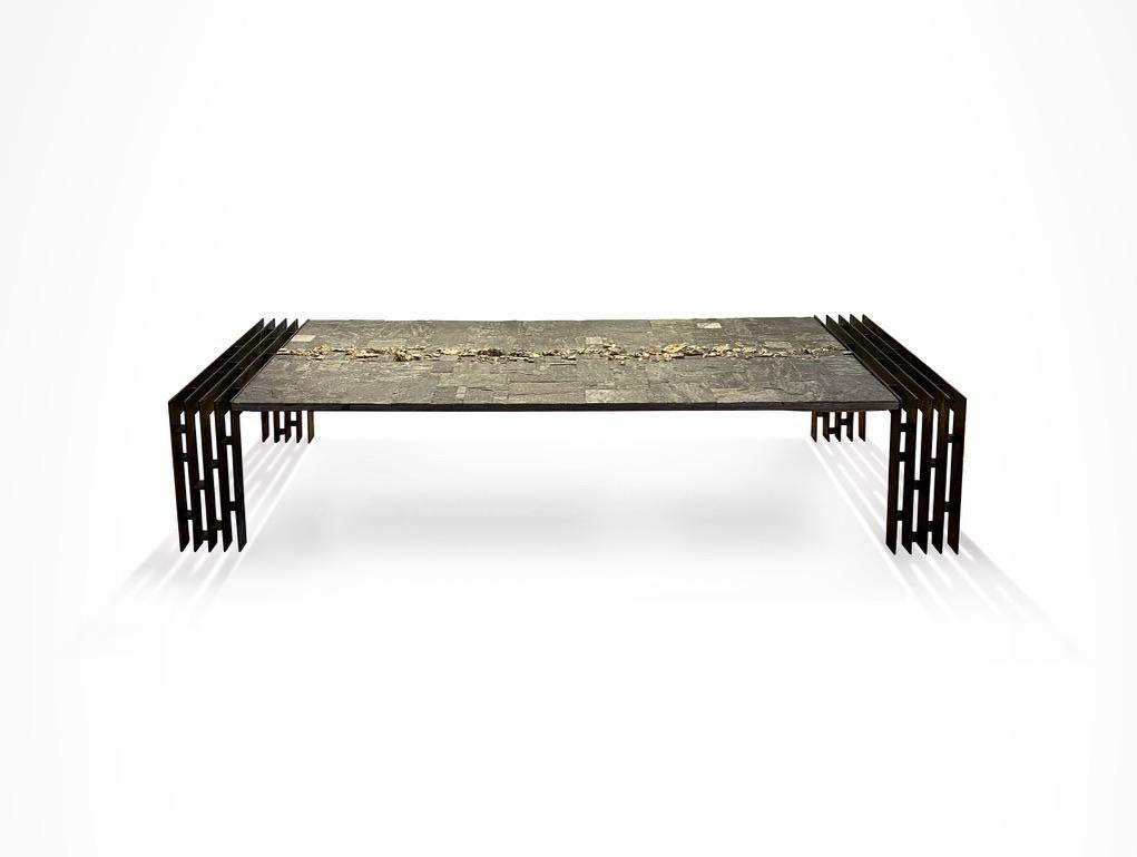 Table top of Brazilian Shiste slate (with natural sparkle inclusions) geometric sections enhanced by a central band of Pyrite elements in high relief. On openwork welded steel legs.
'Pia Manu' plaque set into table top.

The Pia Manu (meaning