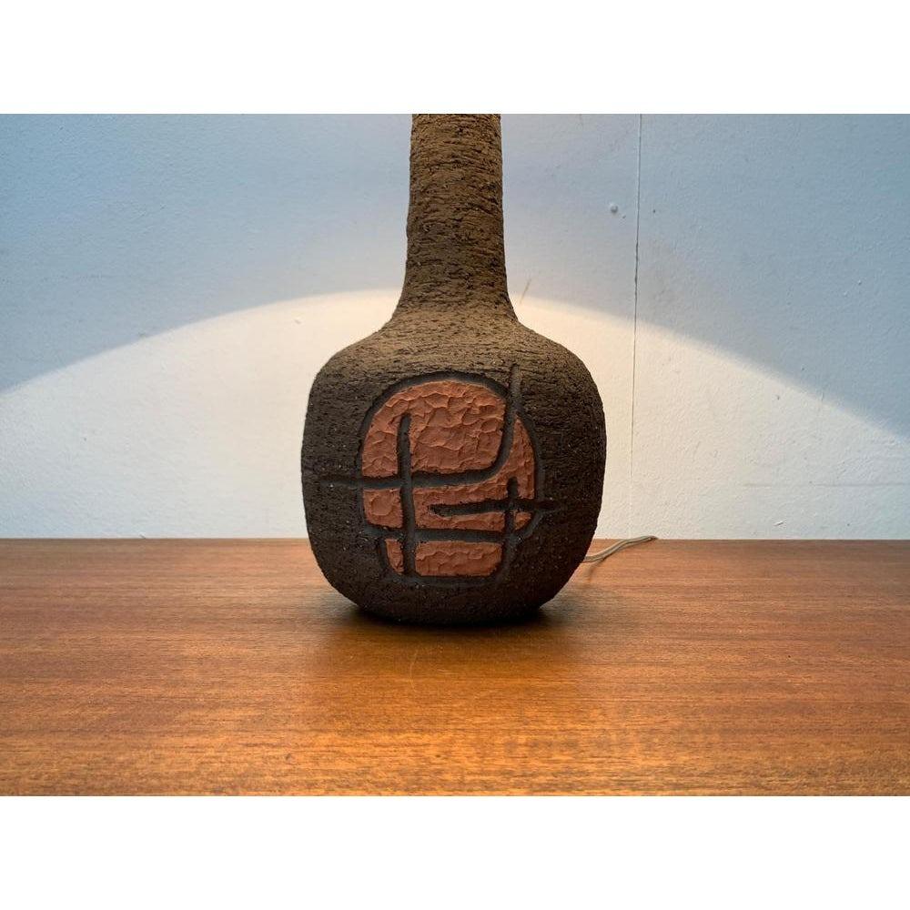 Great Danish studio Pottery table lamp from 1979.

The lamp convinces with its elegant shape. The slim shaft that merges into the bulbous foot is striking. The ceramic foot shows a graphic ornament on the front that is placed in orange. The simple