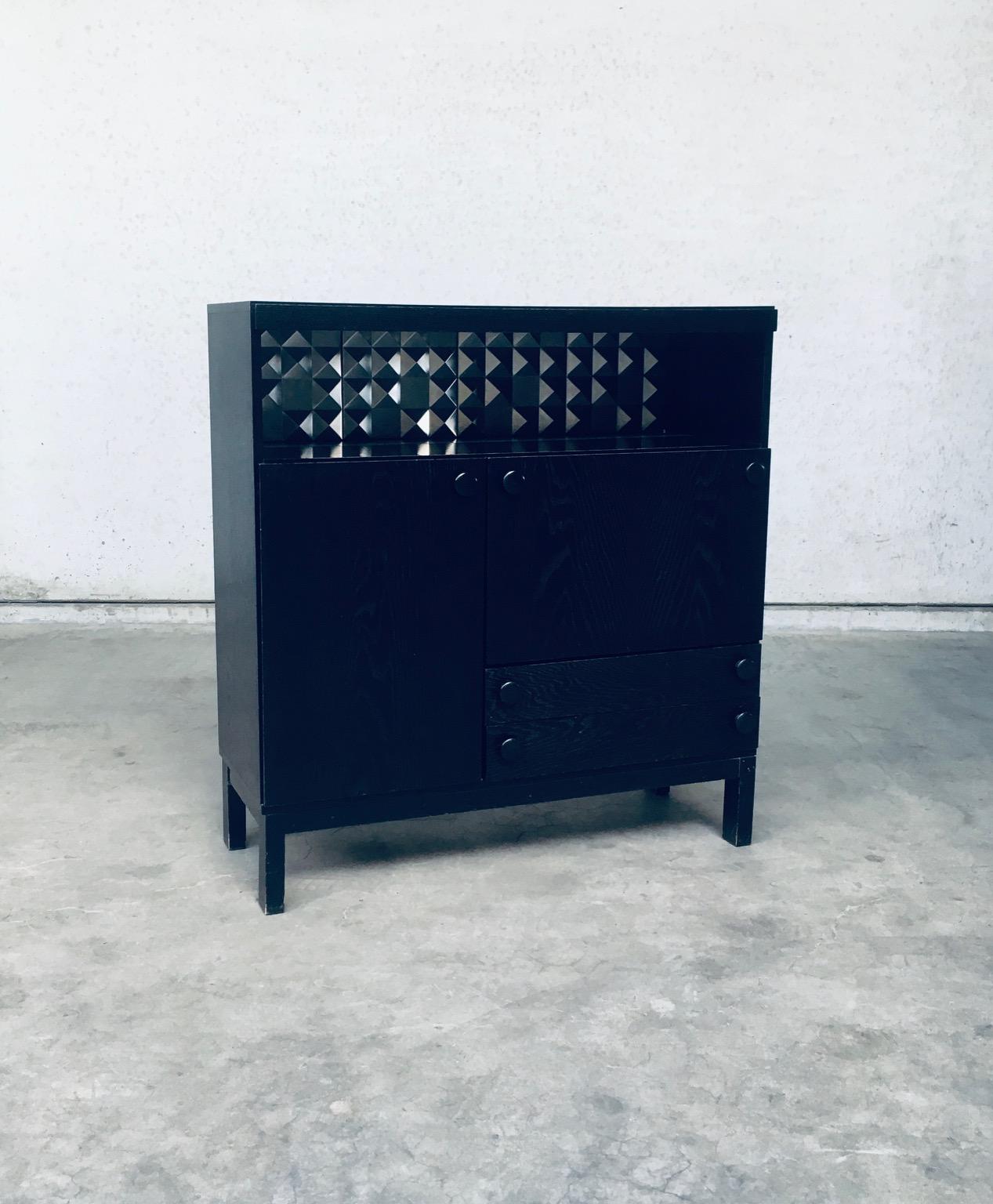 Brutalist Belgian Design Black Ebonized Dry Bar Cabinet. Made in Belgium, 1970's period. No maker markings. In the manner of De Coene Frères Mfg. Black ebonized stained oak with aluminum graphic diamond pattern back plates and back light. This has a