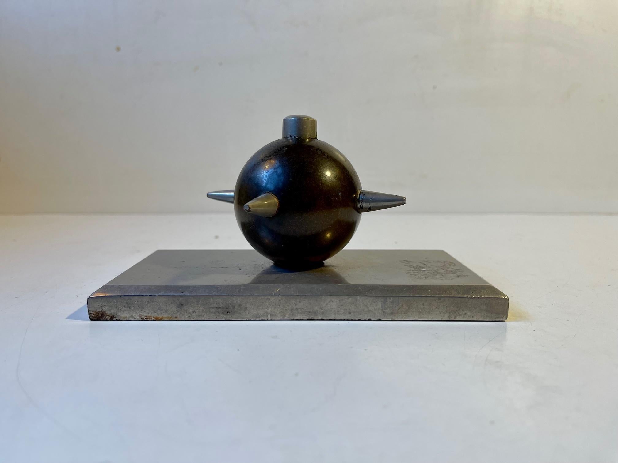 Mit einem Gewicht von über 2 kg wurde diese kleine, einzigartige Schreibtischskulptur in den 1930er Jahren anonym in Dänemark hergestellt. Der dicke Sockel aus rostfreiem Stahl trägt eine Kanonenkugel aus Bronze aus dem 18. oder 19. Jahrhundert, die