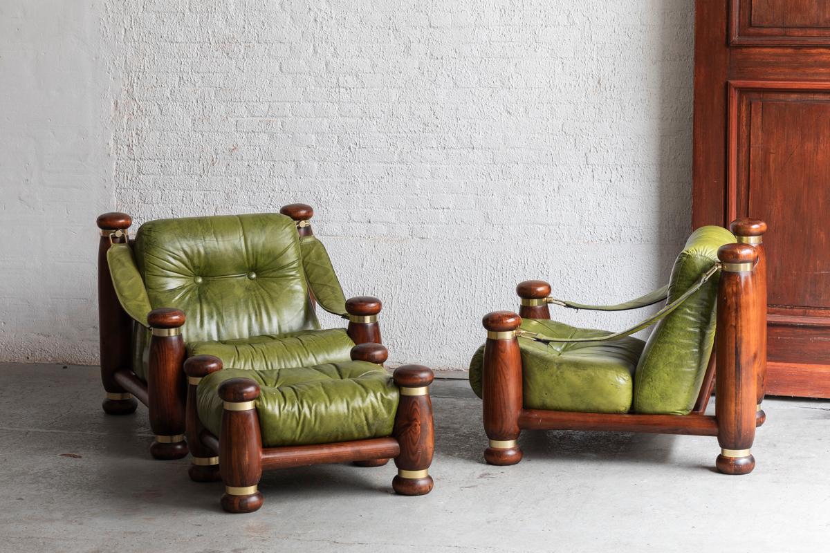Set of two easy chairs designed and made in Italy around 1970. This monumental set features a dark stained pine frame and an olive-green leather upholstery. This royal set comes with a matching hocker. Brass metal rings adorn the dark-stained