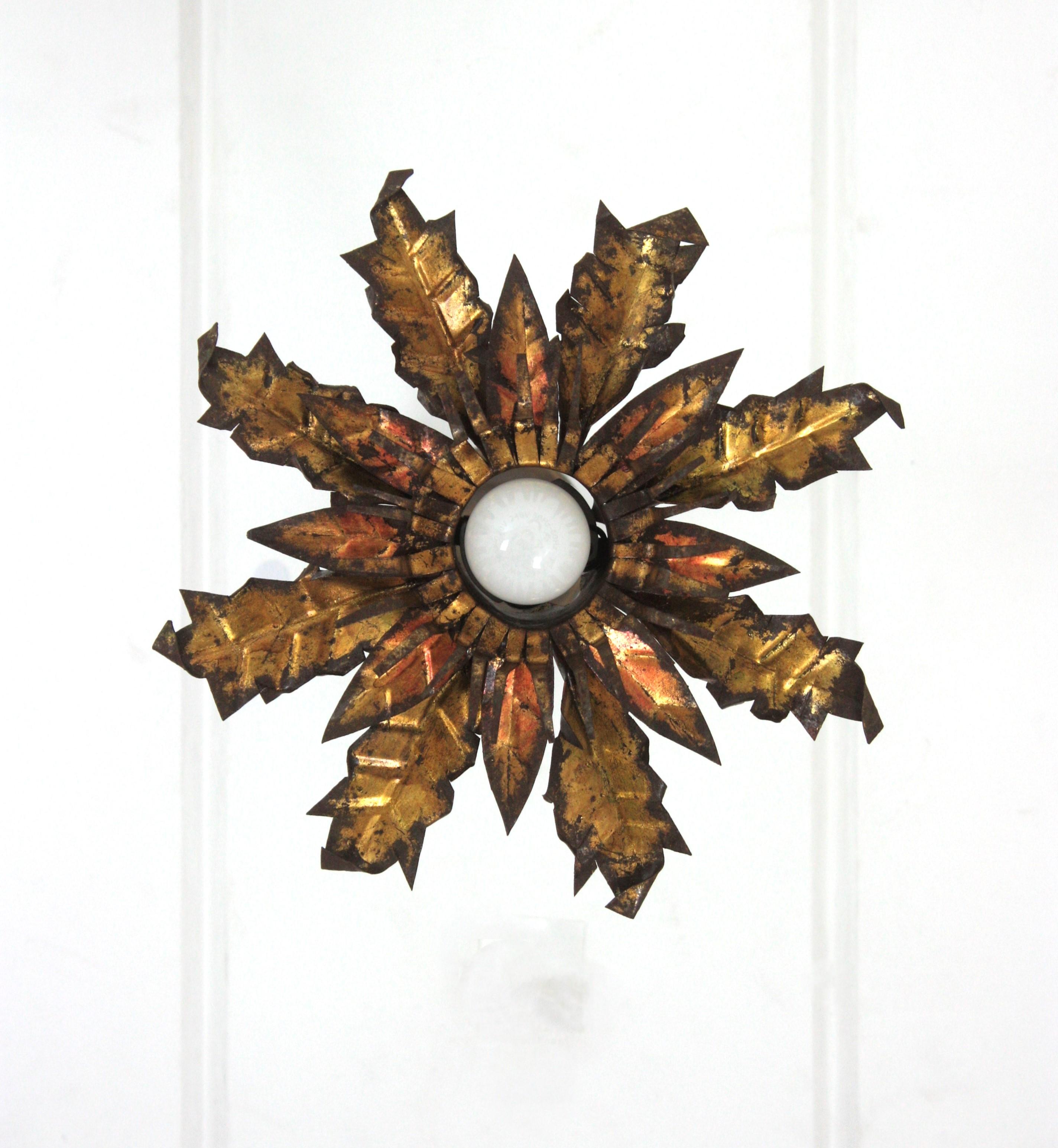 Flor de sol empotrada, hierro dorado, pan de oro, España, años 50.
Esta llamativa luminaria está hecha de hierro cortado a mano y presenta dos capas de hojas doradas en dos tonos que rodean una luz central con una bombilla expuesta. Tiene una pátina