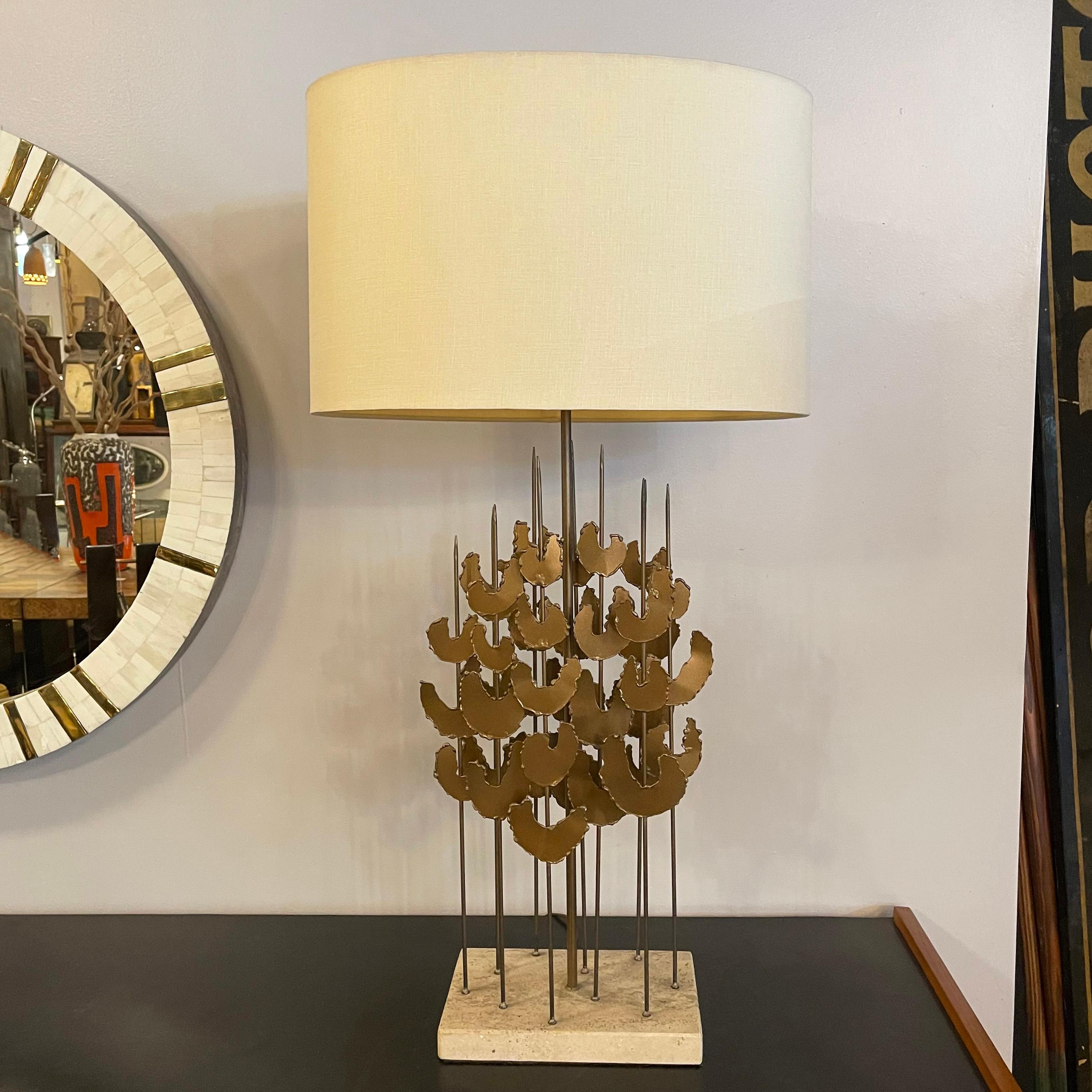 Mid-Century Modern table lamp in the style of Curtis Jeré is as much sculpture as it is lamp with graduated, Brutalist, brass-toned, foliate stems sprouting from a travertine base. The stem portion of the lamp measures 22.5 inches ht.