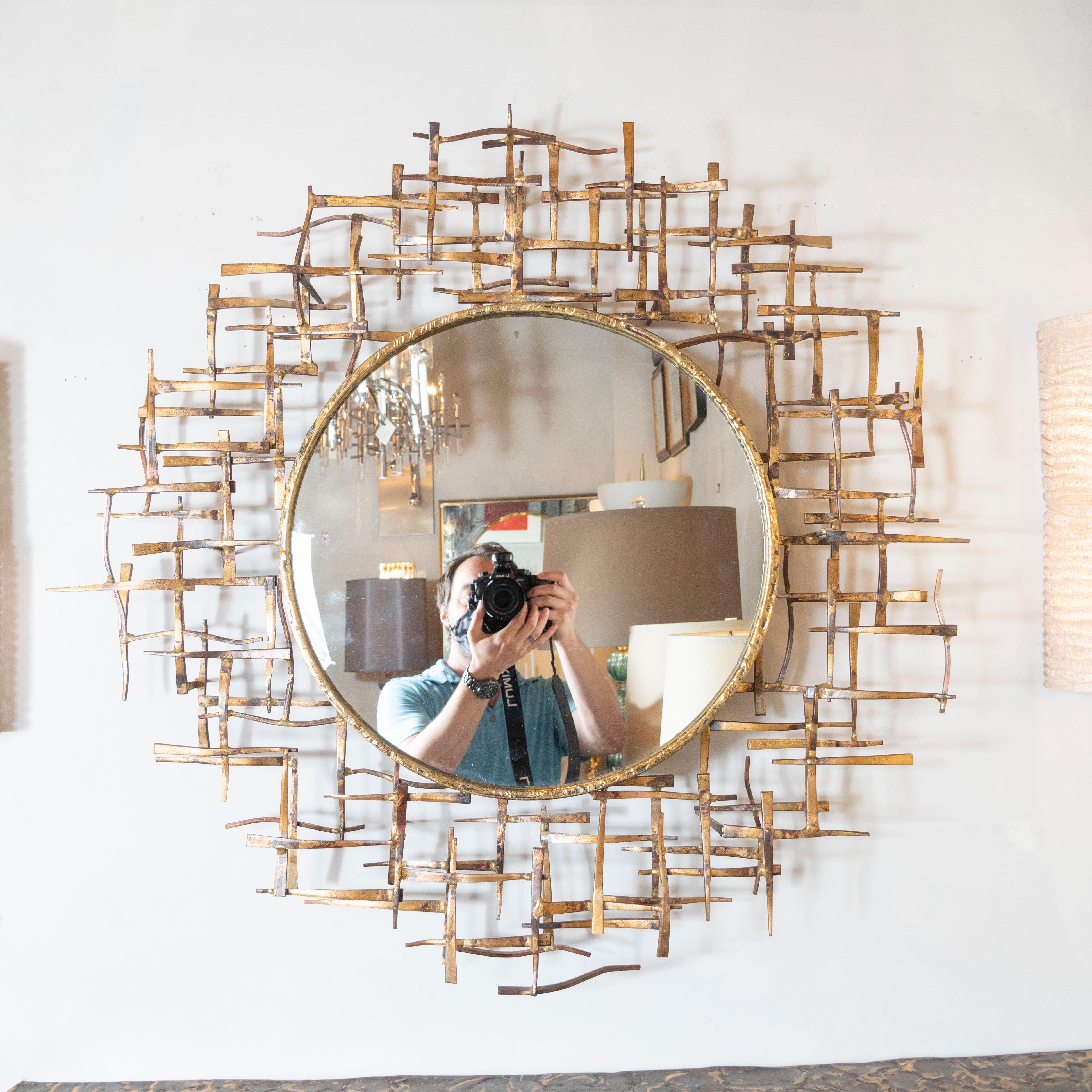 This sophisticated Brutalist wall mirror was realized in the United States, circa 1970. It features a circular bronze wrapped mirror framed by an abstract rectilinear patchwork mosaic in gilded bronze offering an abundance of subtle metallic tones.