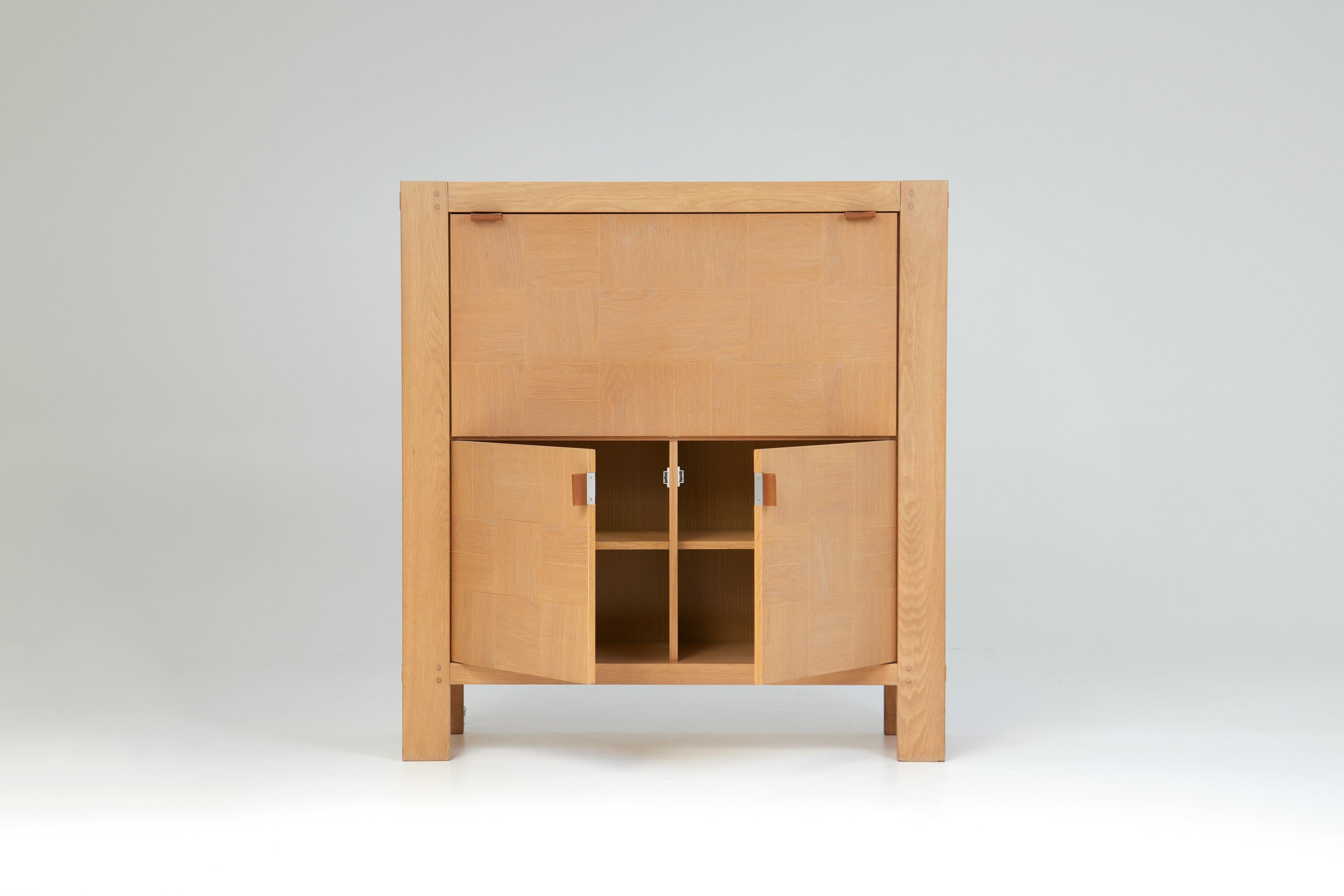 Here we have a highboard with an incorporated bar cabinet, designed by Frans Defour.  
Its doors are beautifully ornamented with oak veneer tiles, giving the highboard a mosaic effect. On the inside we can find multiple shelves, adjustable in