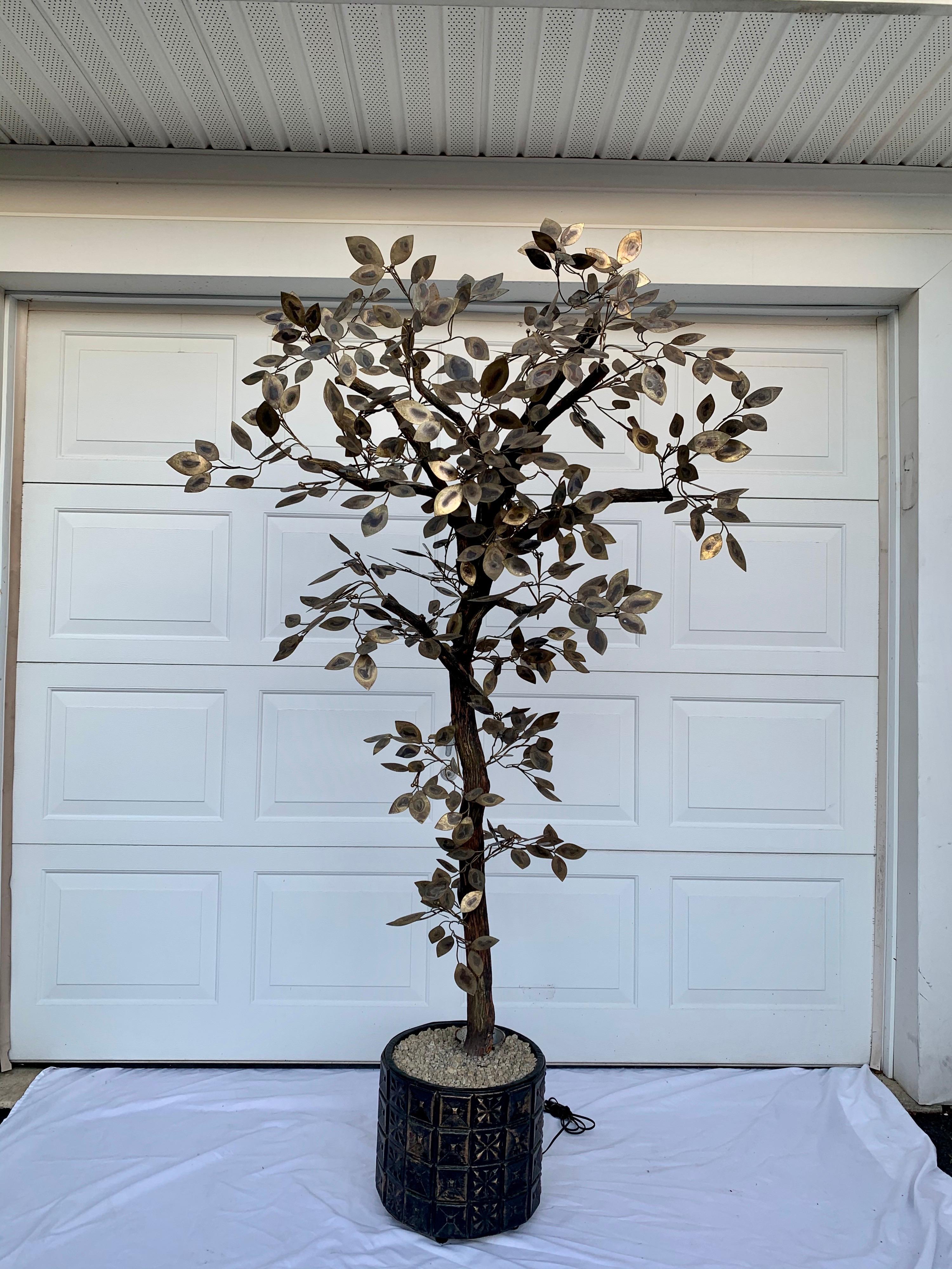 Mid-Century Modern metal tree sculpture by Curtis Jere. This tall dimensional botanic floor tree features torched gold brass metal leaves on natural wood stems and is anchored in a Brutalist planter. The planter has a built-in up light and natural