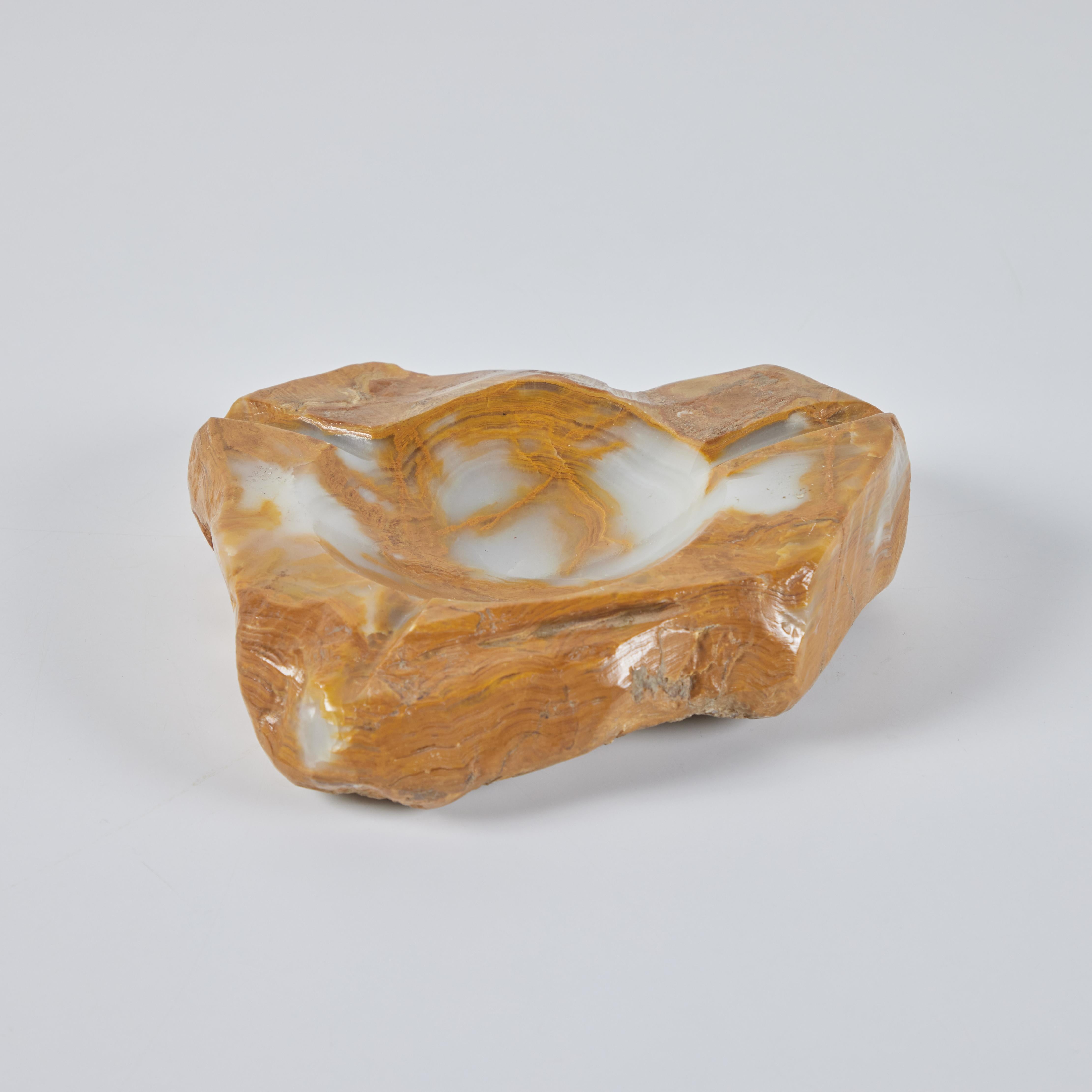 Hand carved polished onyx ashtray features a beautiful golden and cream coloring with a raw edge. The center of the tray has a round dish with three grooves coming off the center. Though initially used as an ashtray, it can serve as a vide poche or