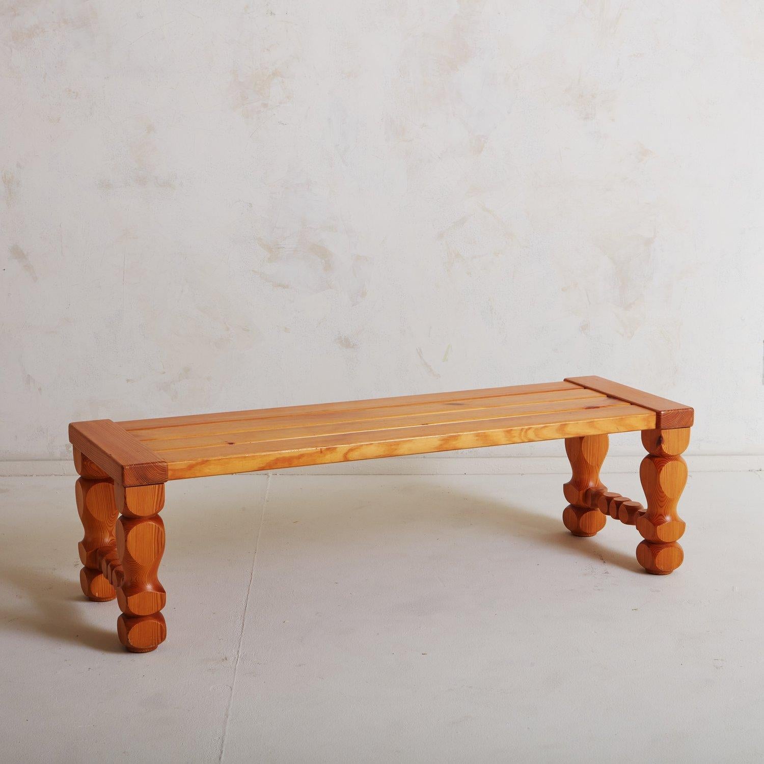 A brutalist 1970s Swedish bench by Glas Mäster Markaryd featuring intricately carved geometric legs with stretcher details. This bench has a slatted top constructed with four pine boards. We love the sculptural detailing and rich graining on this