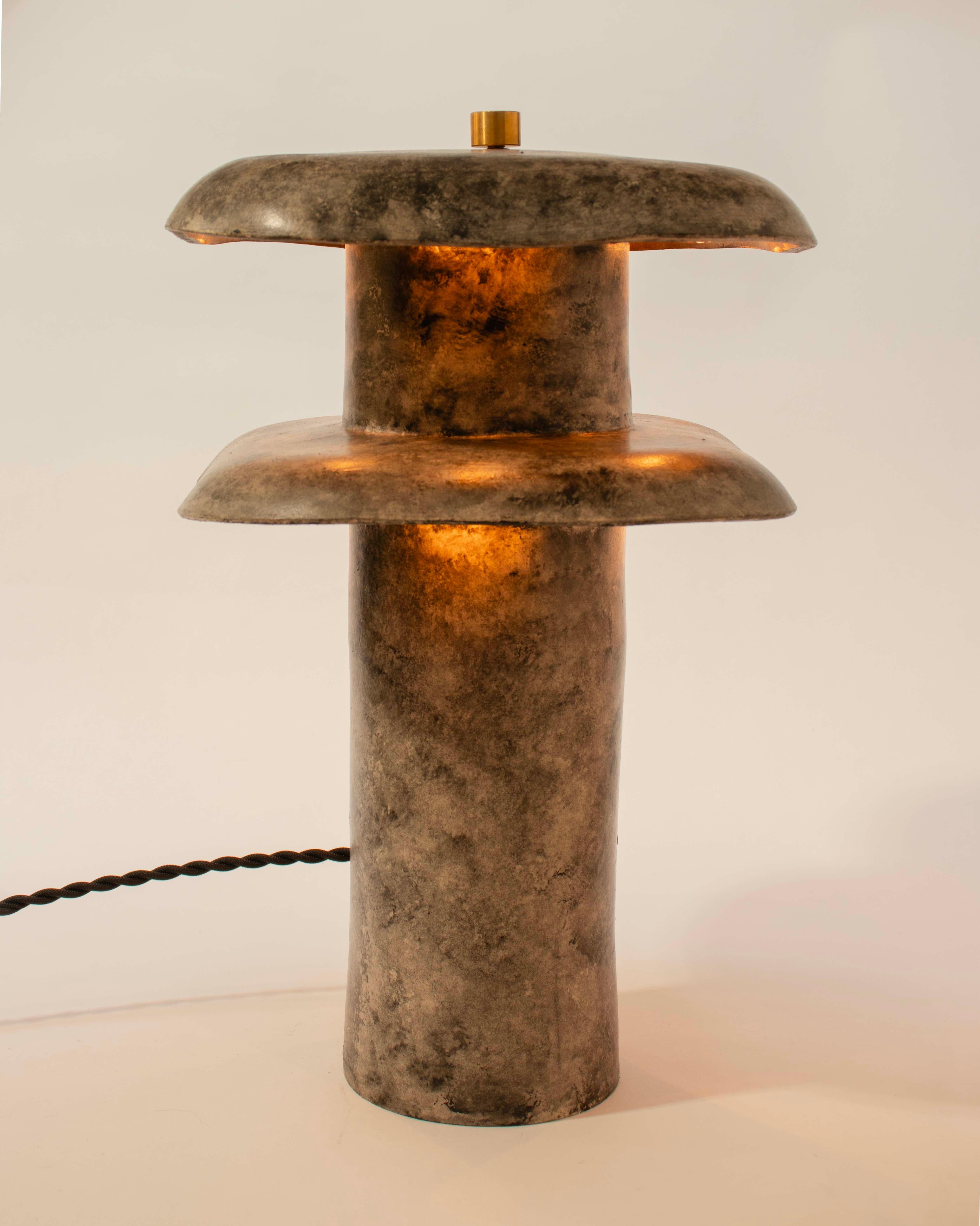 The Double Decker lamp is a tall, brutalist-inspired table lamp, perfect for lighting in larger living spaces, created by Streicher Goods in Brooklyn, NY. 

The lamp is composed of a vertical, cylindrical base that supports two large, overlapping,