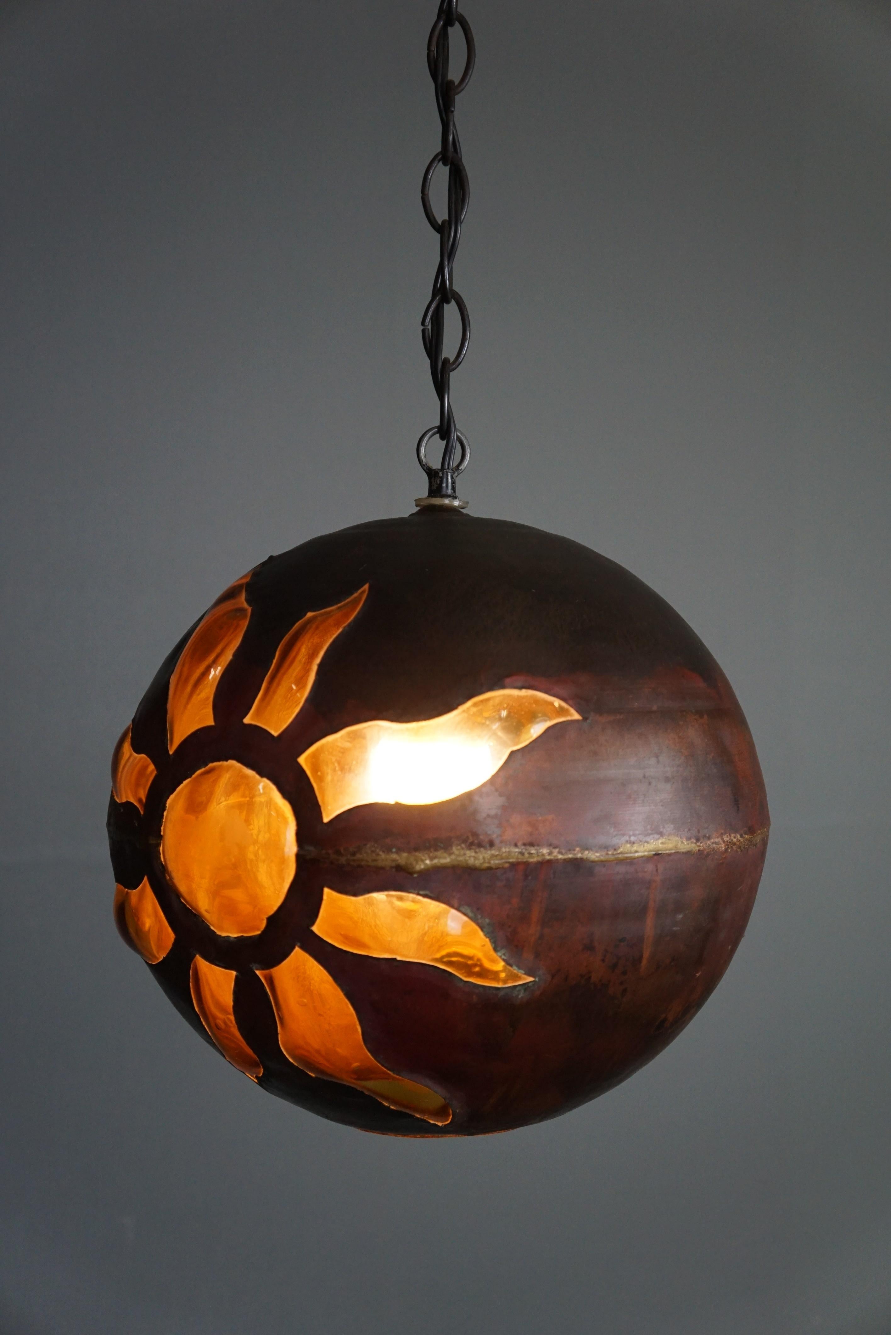 This Mid-Century Brutalist hanging lamp designed by the Finnish designer Nanny Still McKinney in the 1960s.

This rustic and unique hanging lamp from Nanny Still-McKinney is made of patinated copper in which a blown amber-colored glass interior has