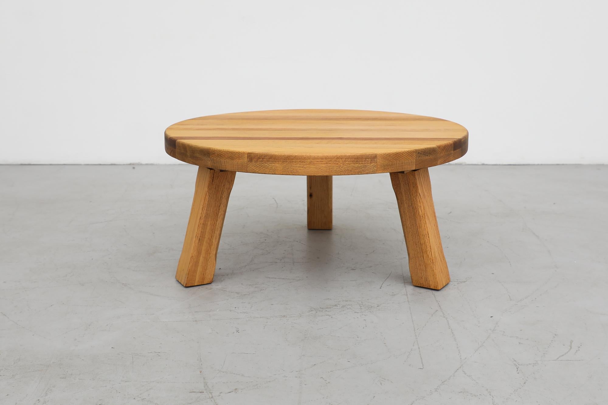 This heavy round Brutalist coffee table is made from solid oak with a waxed finish. The table has three sturdy square tripod legs with carved detail down the sides. Sanded, refinished and hand waxed, in otherwise original condition with visible wear