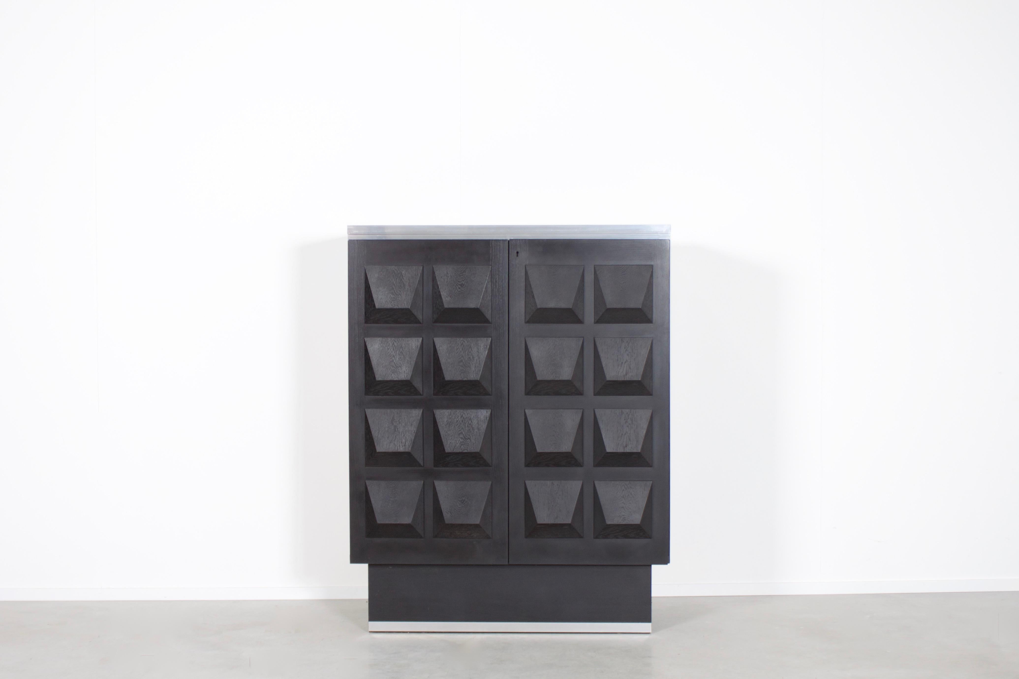 Impressive Belgium Brutalist cabinet in very good condition.

This sideboard has two doors made of massive black stained oak, each with a three-dimensional pattern. 

On the top and bottom the cabinet is finished with aluminum details. 

Behind the