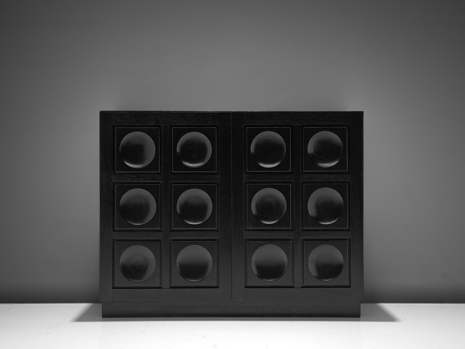 Brutalist highboard, black stained wood, Europe, 1970s. 

Modern and clean highboard with two-door panels. Each door is executed with an exceptional three-dimensional pattern of squares and circles. The continuous pattern gives this bar-cabinet a