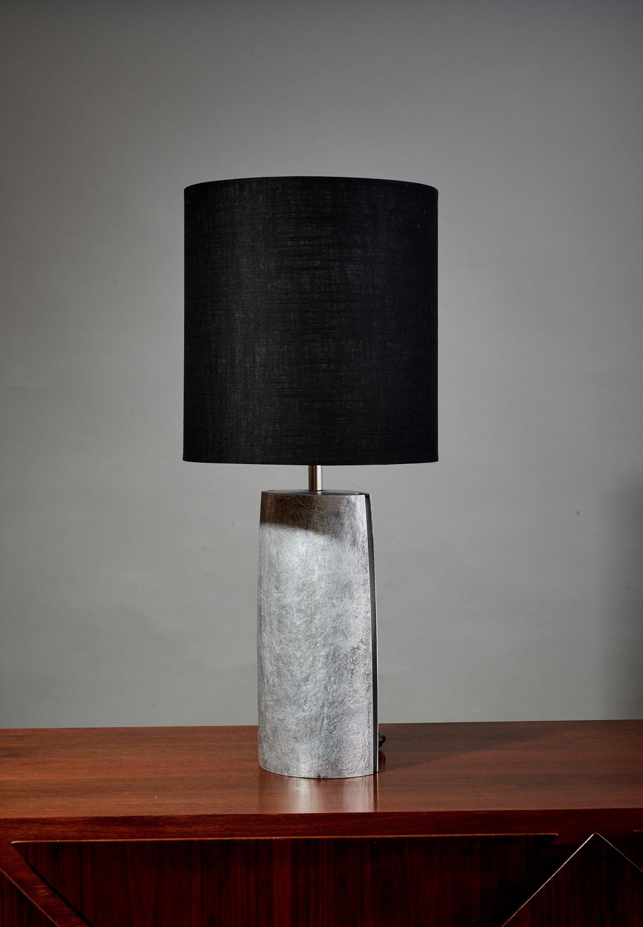 Italy, 1970's

A large, Brutalist table lamp in solid textured aluminum, monolithic in form. The elipse-shaped base tapers at either end to fine points routed by a deep groove. With a cylindrical chrome finial. The lamp's industrial materials are