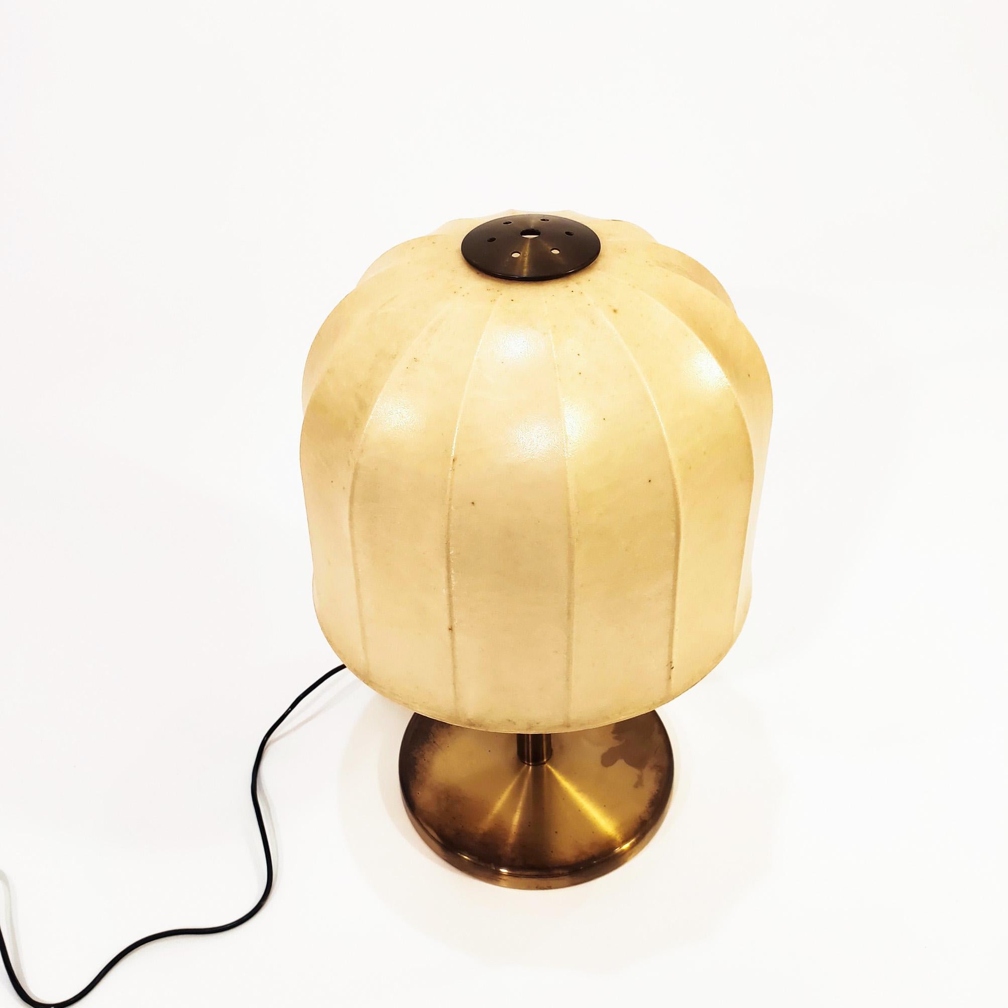Italian table lamp from the 70s. The body and structure are made of polished brass, and the upper shade is made of a metal frame covered with cocoon resin. 
The material of cocoon was invented after World War II to protect unarmed warships and other