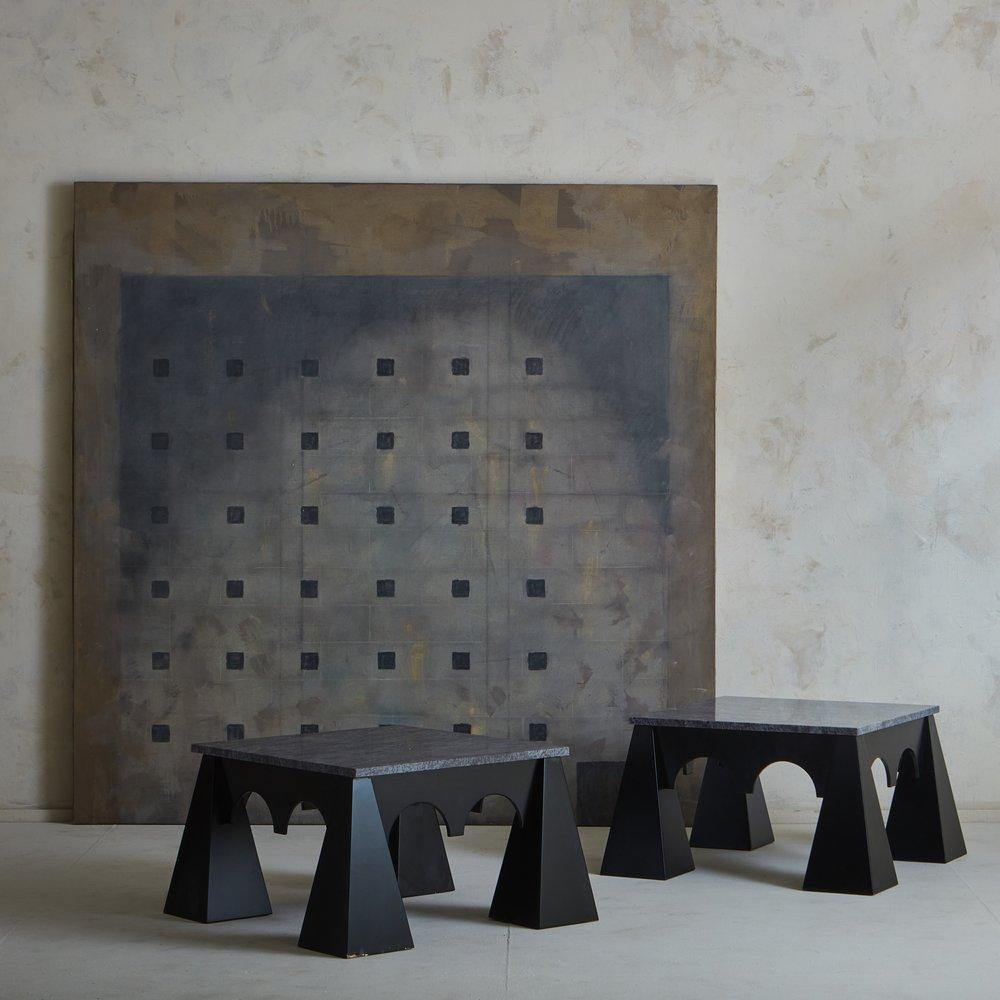 A 1980s Italian brutalist coffee table with a sculptural black lacquered wood base and a square marble top. The marble has a range of gray and blue hues with beautiful veining. This table stands on four dramatic, triangular legs and features