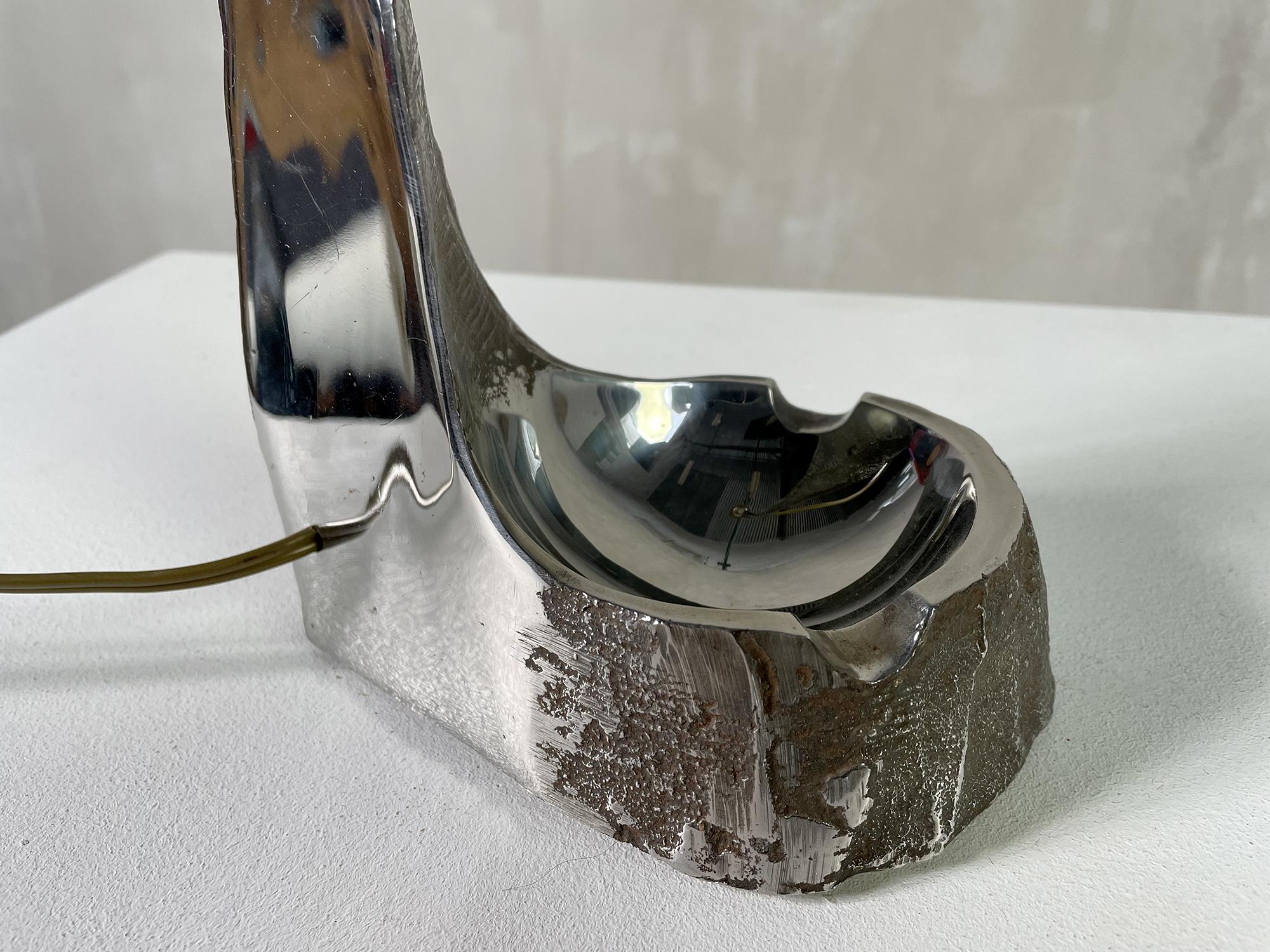 Grande lampe brutaliste en acier inoxydable massif, France 1970. Le bloc de métal a été travaillé dans la masse, poli miroir d'un côté et brut de l'autre. Un bol/cendrier forme la base. Cette lampe sculpturale est une pièce unique.
Mesure : hauteur