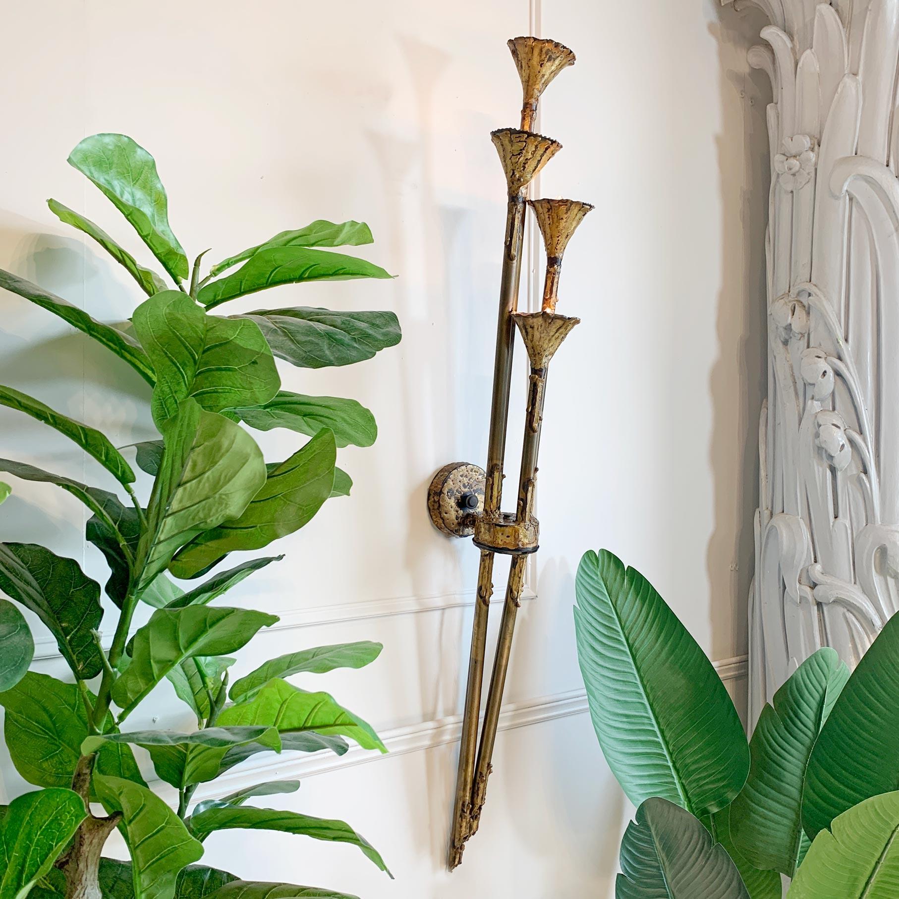 An outstanding Brutalist movement handcrafted torch cut brass torchiere wall light by Tom Greene, circa 1970. This architectural and sculptural wall light for The Feldman Company has 4 trumpet lamp holders, each with a single E12 bulb holder.

Of