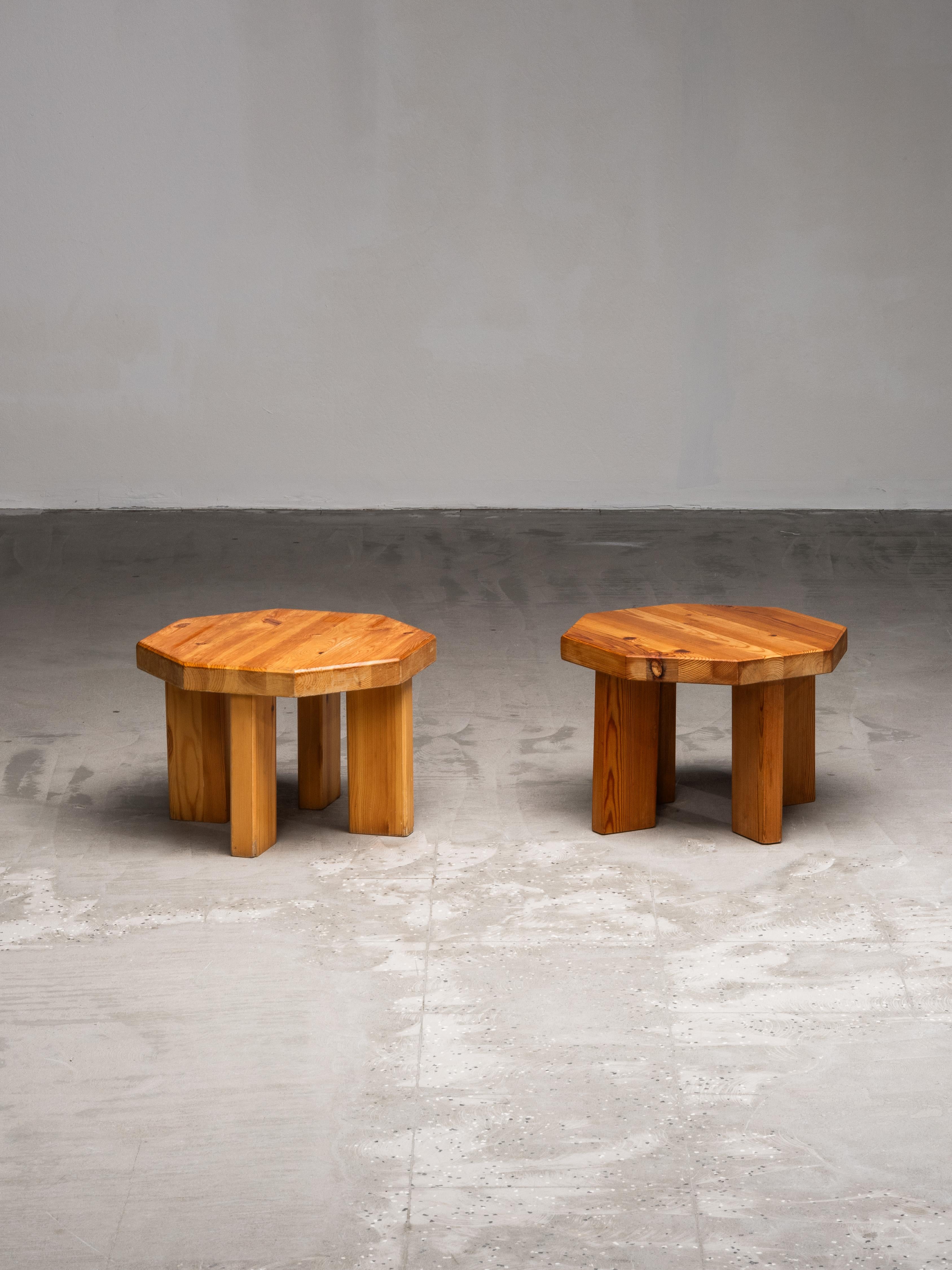 A pair of low, octagonal stools crafted from solid pine, produced in the 1970s. Each piece features a thick, faceted top resting on four chunky, vertical legs — a construction that gives them a grounded, architectural presence. The warm tone of the