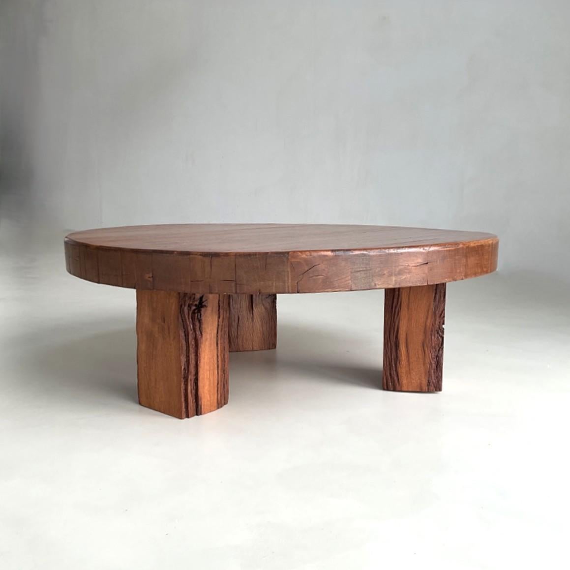 An artisan 1970s solid oak coffee table featuring a thick, sculptural tabletop supported by three rustic legs. Slightly lower than standard height, the piece embodies a Wabi Sabi aesthetic with its understated, organic presence. It is in good