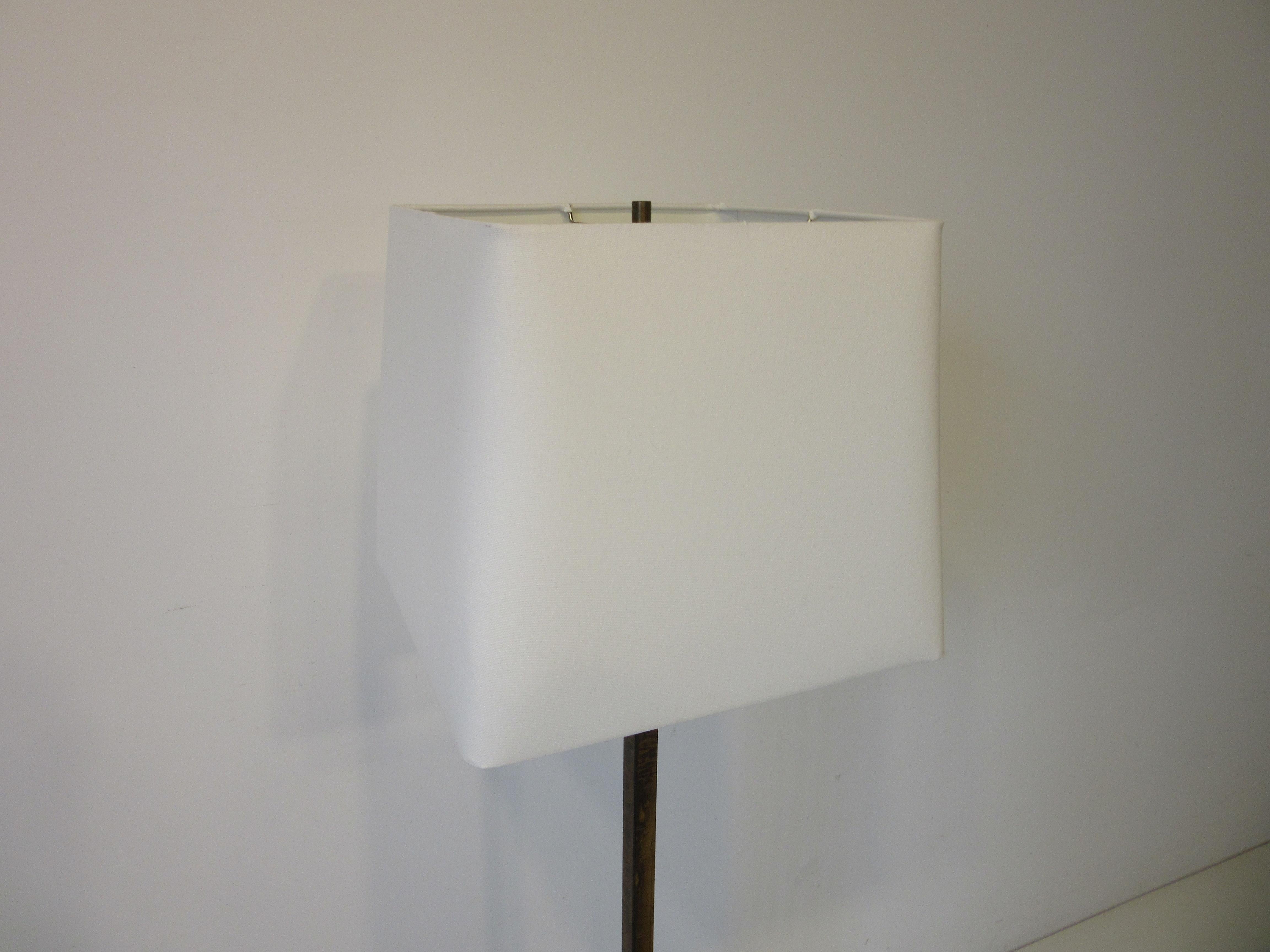 A Brutalist styled metal floor lamp with tapered base going into a square shaft topped with a cream square linen shade, manufactured by the Laurel Lamp Company.