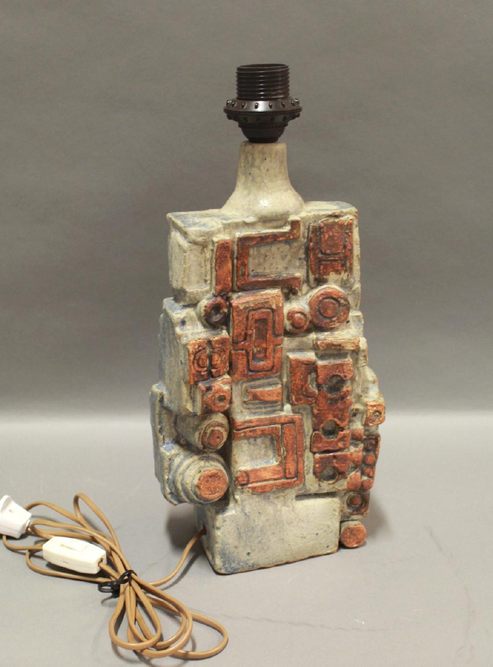 This brutalist mid-century modern stoneware table lamp with matte cream white and terracotta-colored glaze and relief decoration, was crafted by the renowned artist Bernard Rooke, born in 1938.

It was made in Rooke's own studio in Swilland,