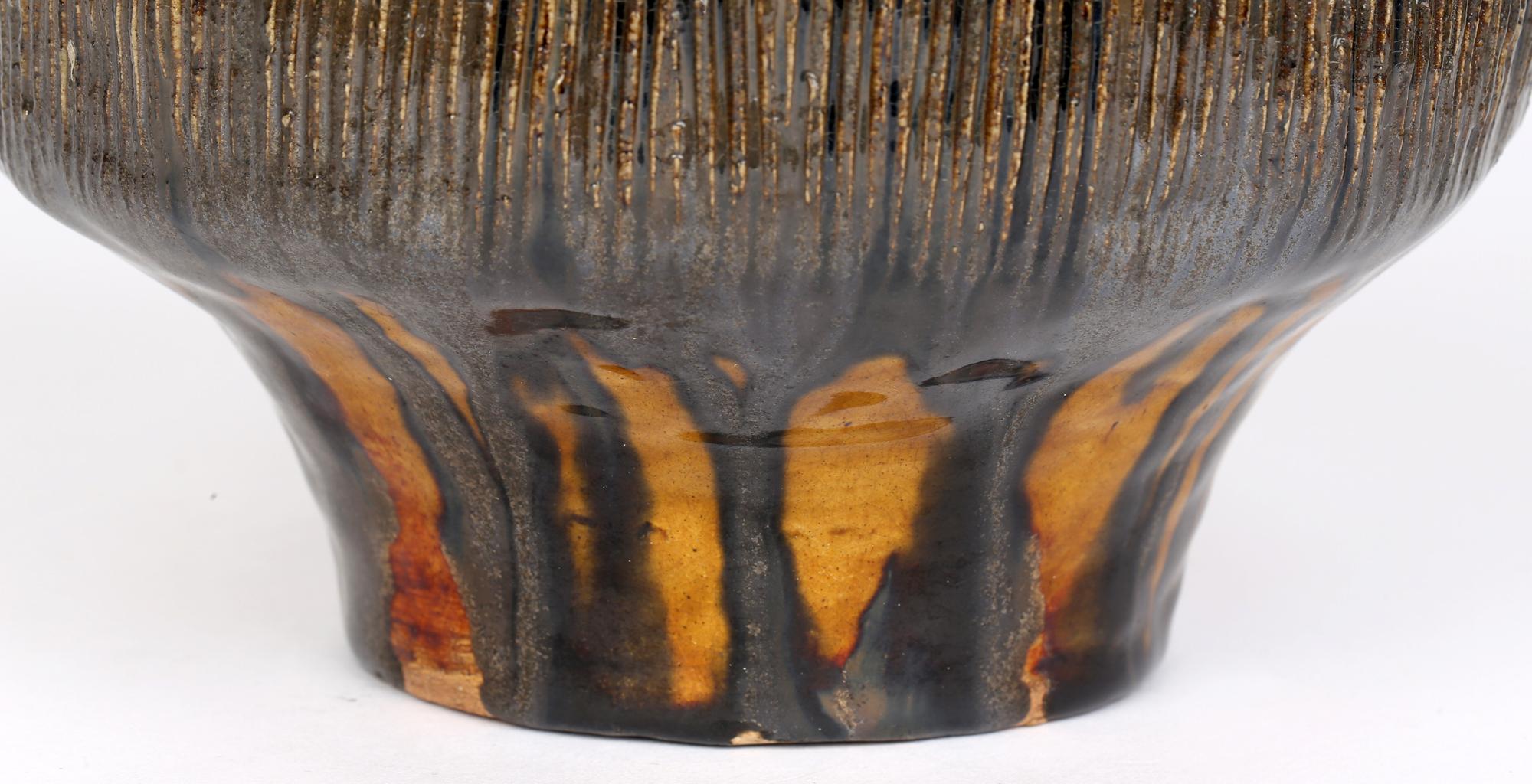 Un vase très élégant en poterie d'atelier du milieu du siècle dans le style brutaliste décoré de glaçures striées jaunes et vertes. Ce vase en grès très travaillé repose sur une base ronde plate et étroite, avec un corps inférieur étroit qui