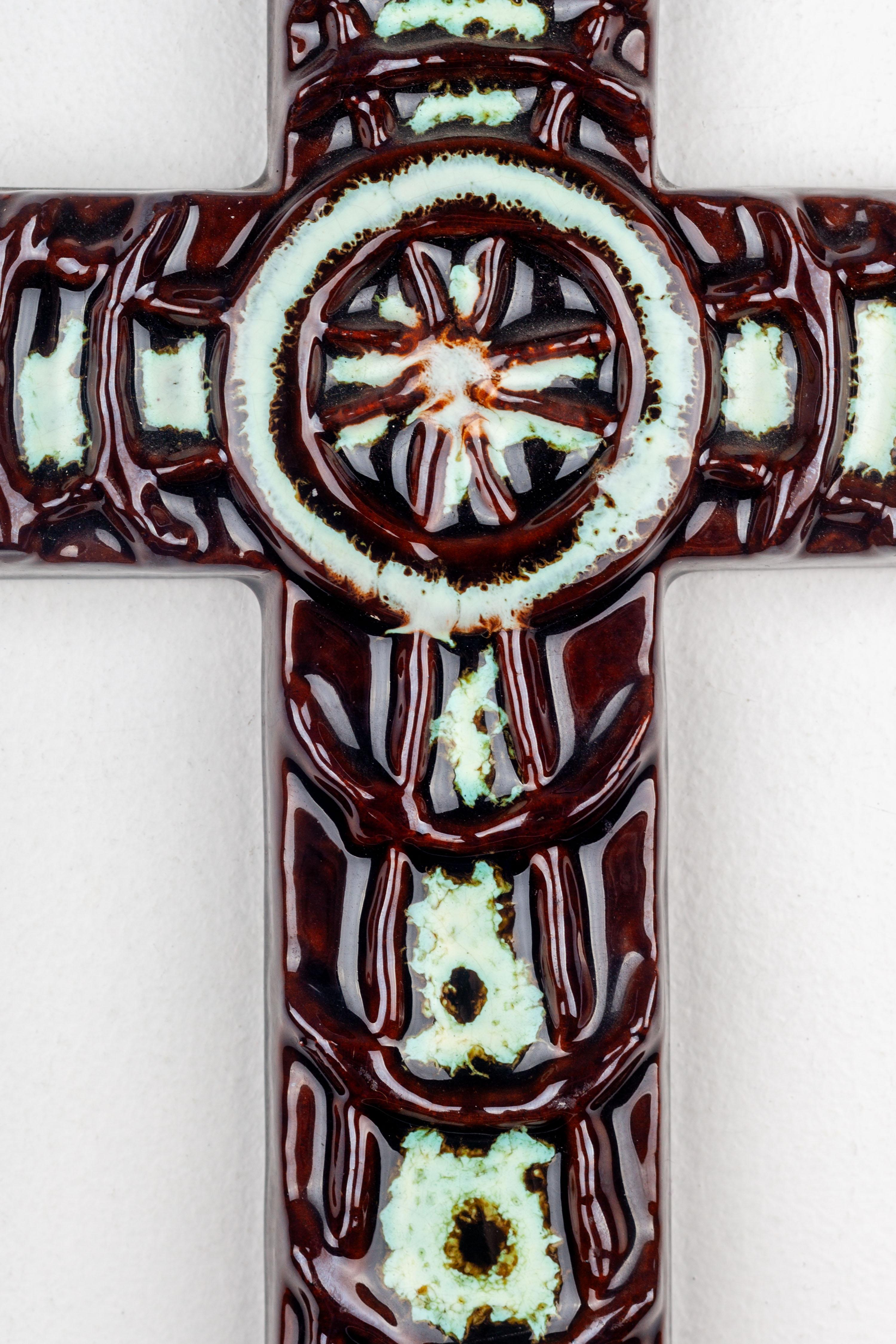 This handmade ceramic wall cross, crafted in Europe during the midcentury period, exemplifies the Brutalist aesthetic. Adorned with concentric circles relief in glossy brown and light green colors, the cross exhibits a simple yet impactful