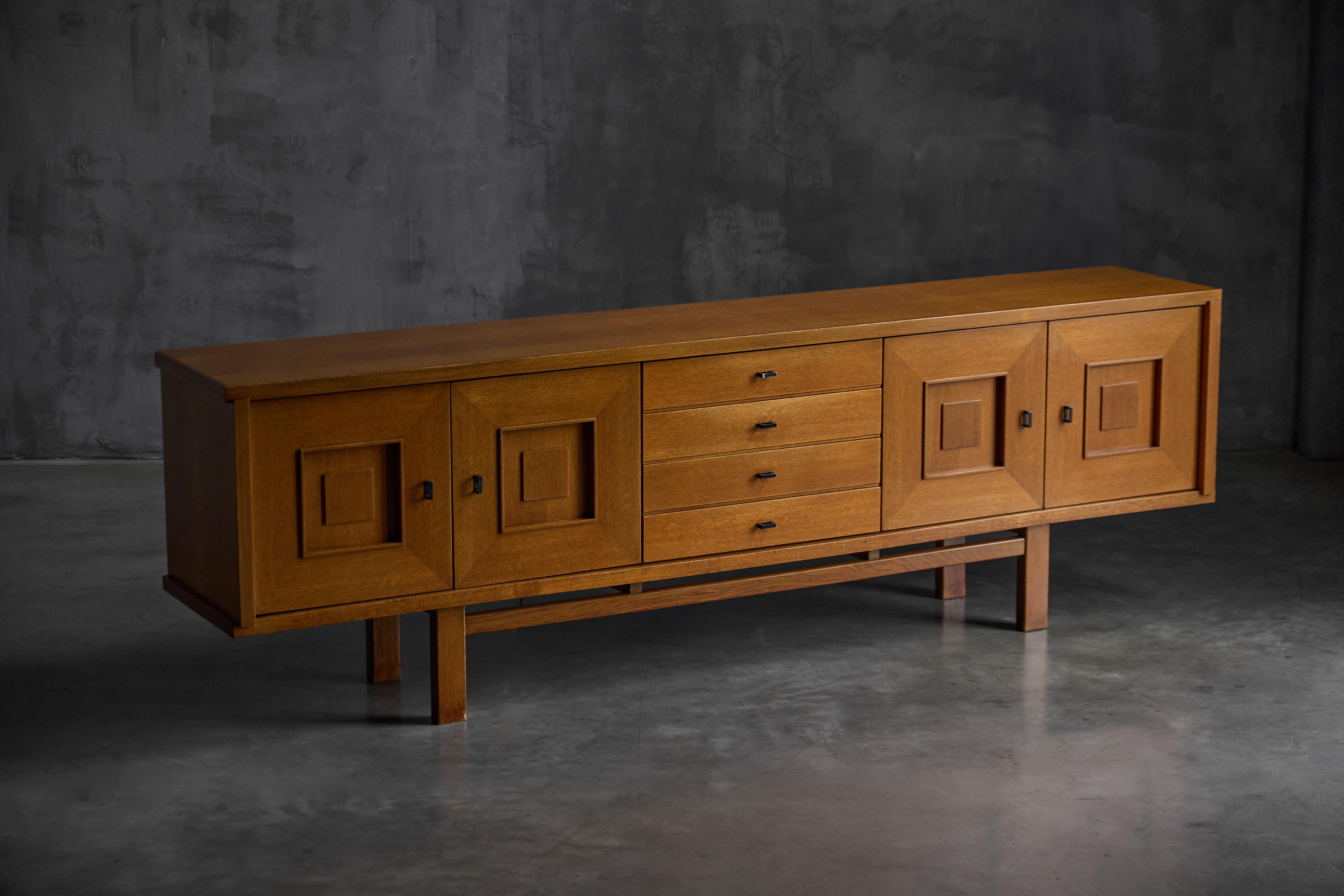This striking brutalist Belgian oak sideboard, model 187/9, embodies the refined craftsmanship and geometric elegance of 1960s furniture design. Constructed from solid and veneered oak, the piece features a symmetrical façade with four central