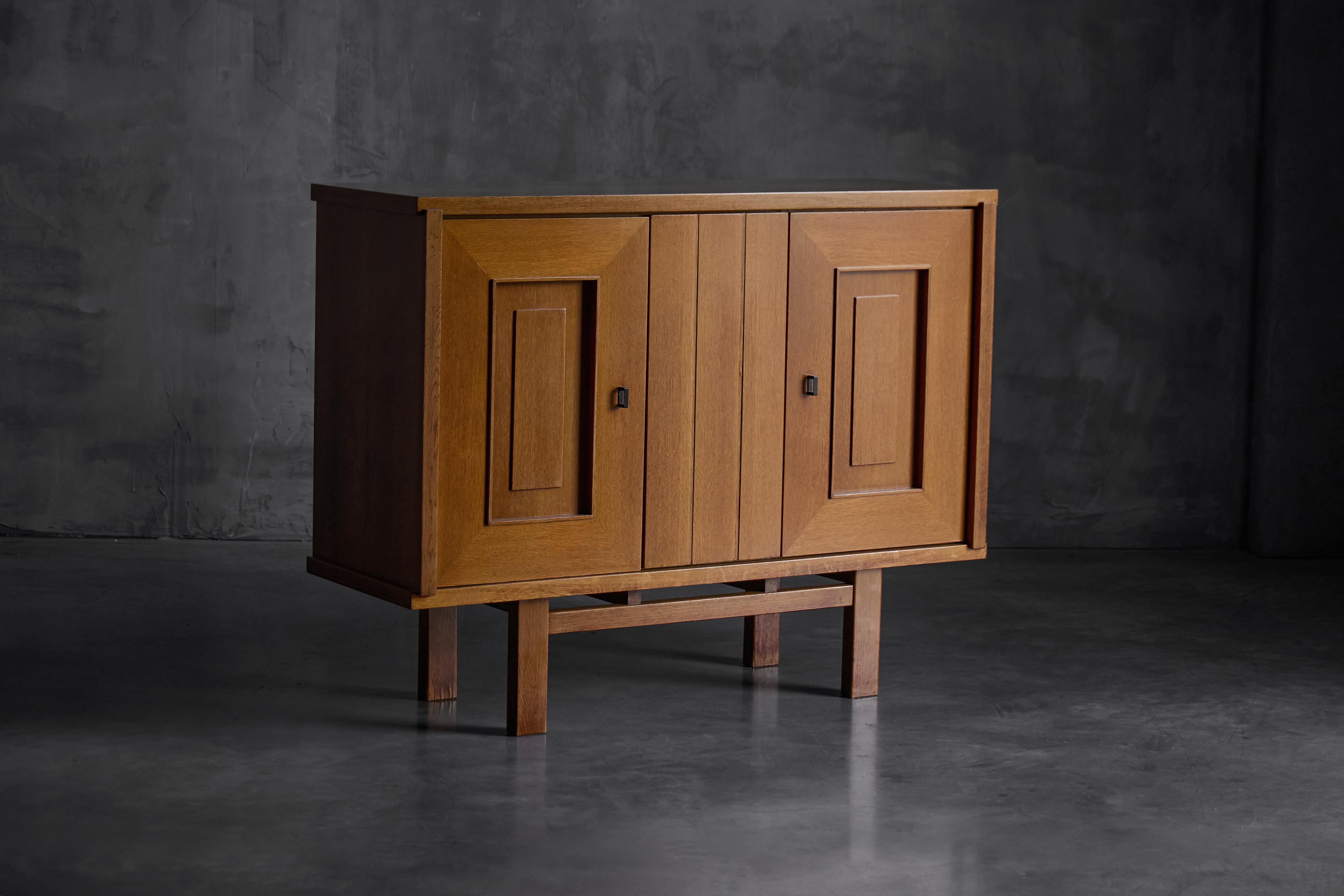 This oak cabinet, model 187/3, is a refined expression of Belgian Brutalist style from the 1960s. Crafted from solid and veneered oak, the cabinet features a balanced façade with two outer doors accented by recessed rectangular panels, framing a