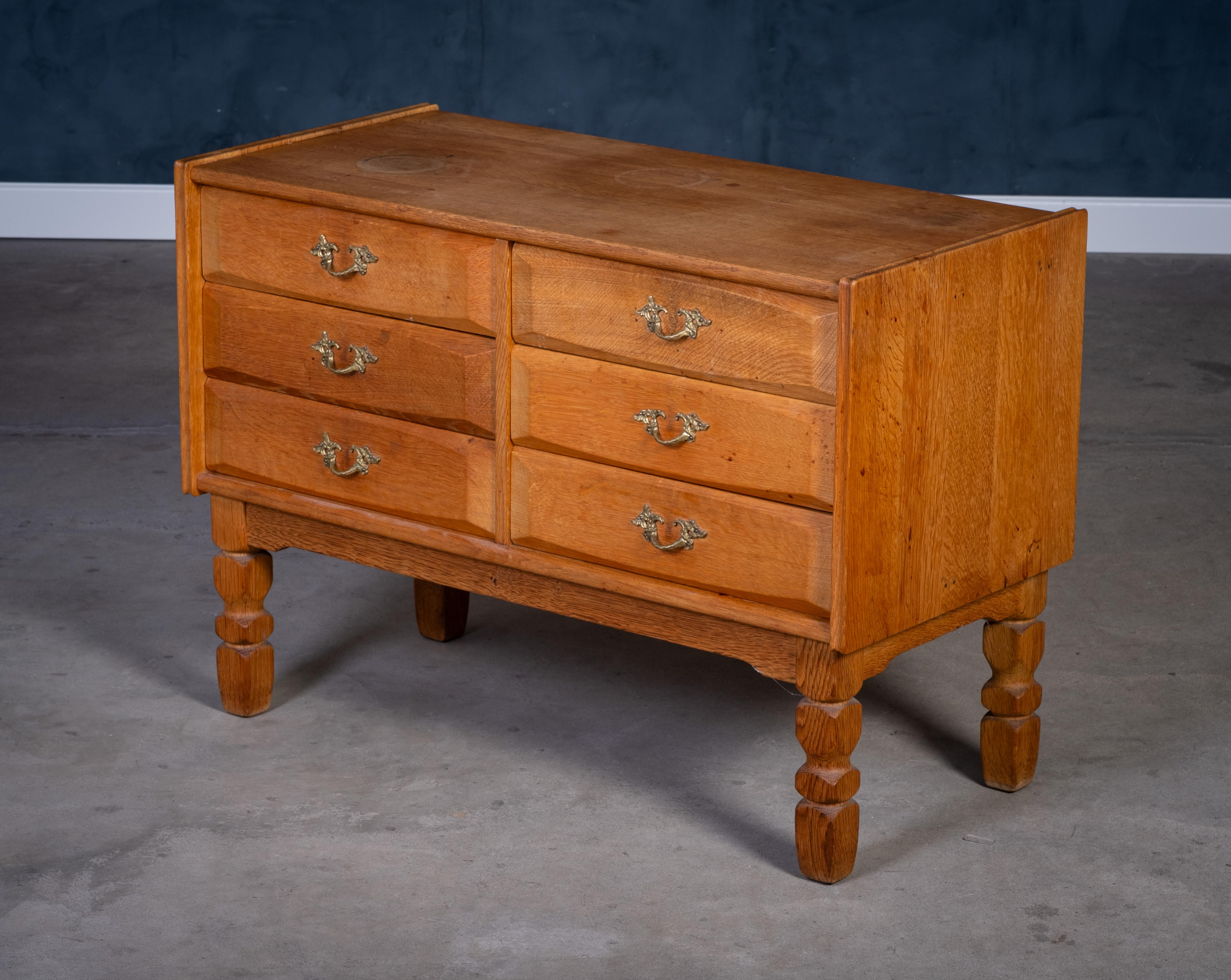 Solid oak chest of drawers, in the style of Henning Kjærnulf, 1970s. A beautiful example of Danish brutalist design with striking carved drawer fronts, six spacious drawers, and elegant brass handles.

Good vintage condition with minor signs of use