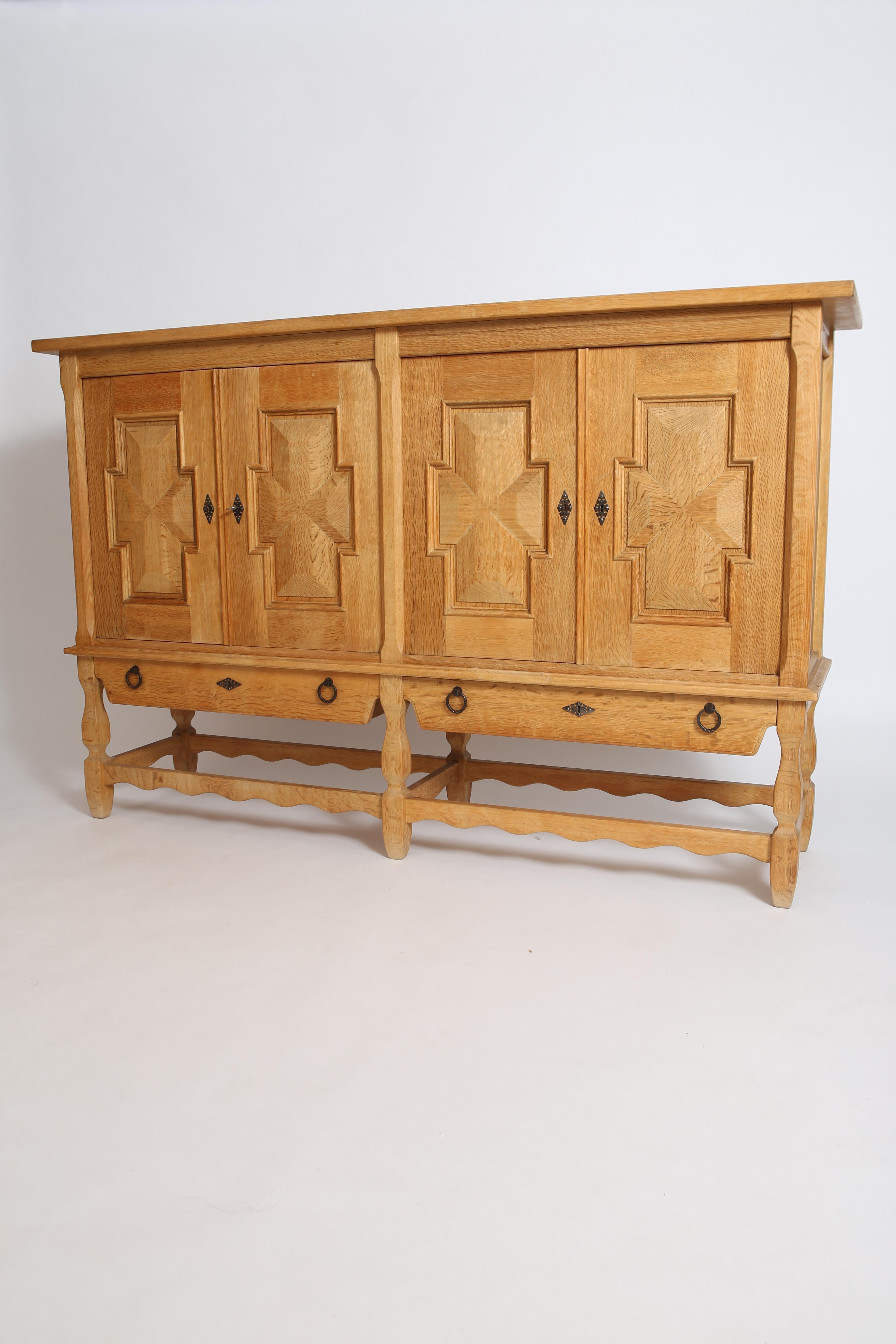 Grand sideboard in solid Oak by Henry (Henning) Kjaernulf. Denmark, circa 1960s. With beautifully ornate carved doors, turned oak legs, and whimsical detailing throughout, this is a statement piece. Patinated brass hardware. Original finish to the