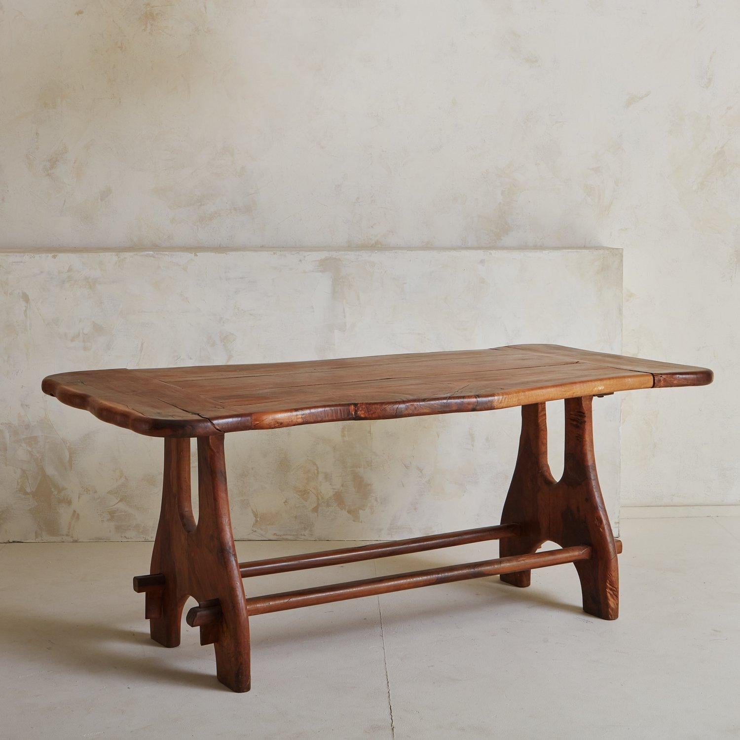 A vintage brutalist French dining table constructed with olive wood. This stunning table features curved legs with decorative cutouts and two stretchers. The tabletop has beautiful curvilinear edges. We love the rich color and graining on this olive