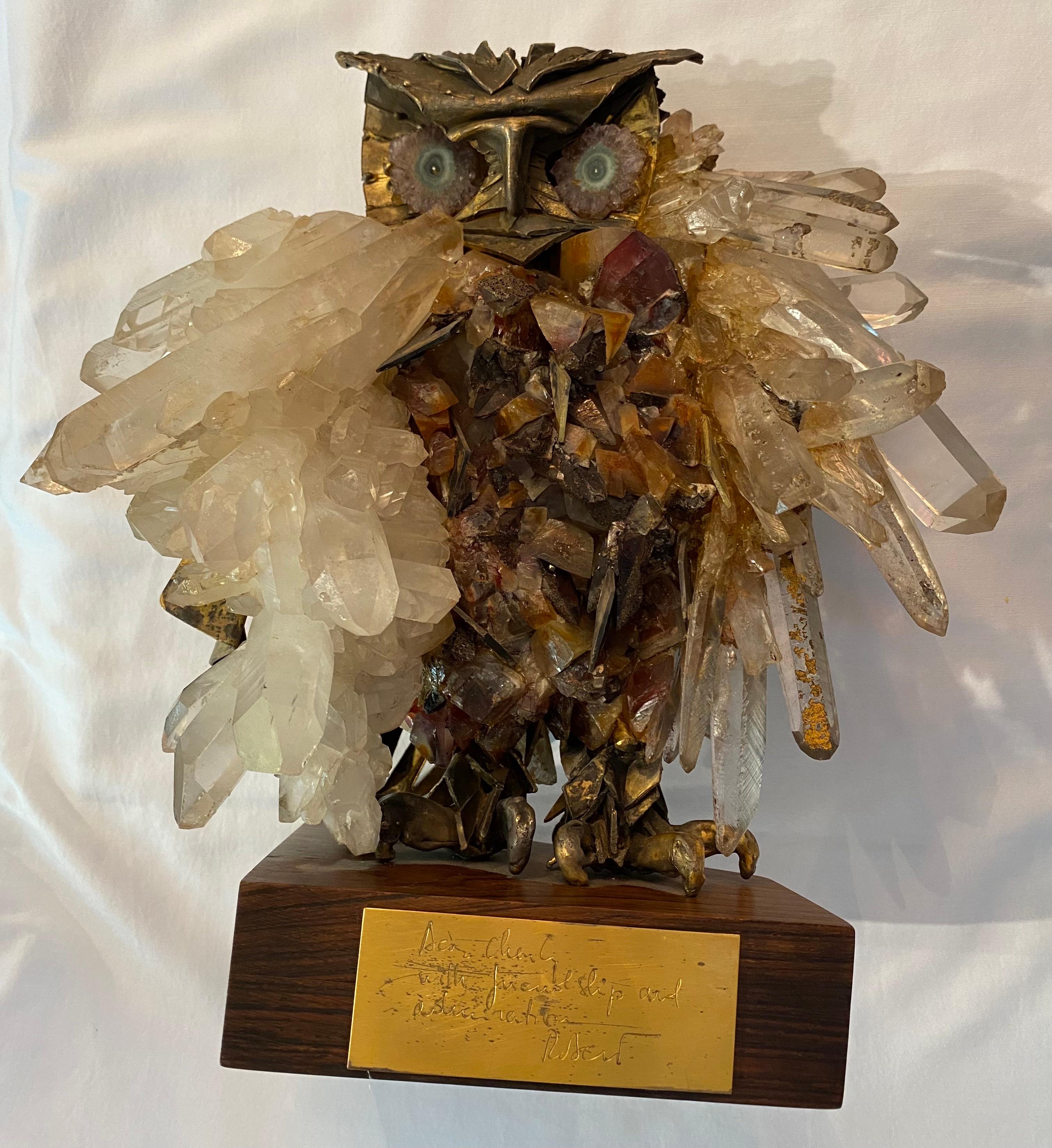 A brass, crystal, and geode Brutalist style sculpture of an owl on a wood base. Most likely done by Artist Claude Barbat. Highly detailed and intricate. The body is formed from hand cut brass and iron stained quartz. The wings are clusters of quartz