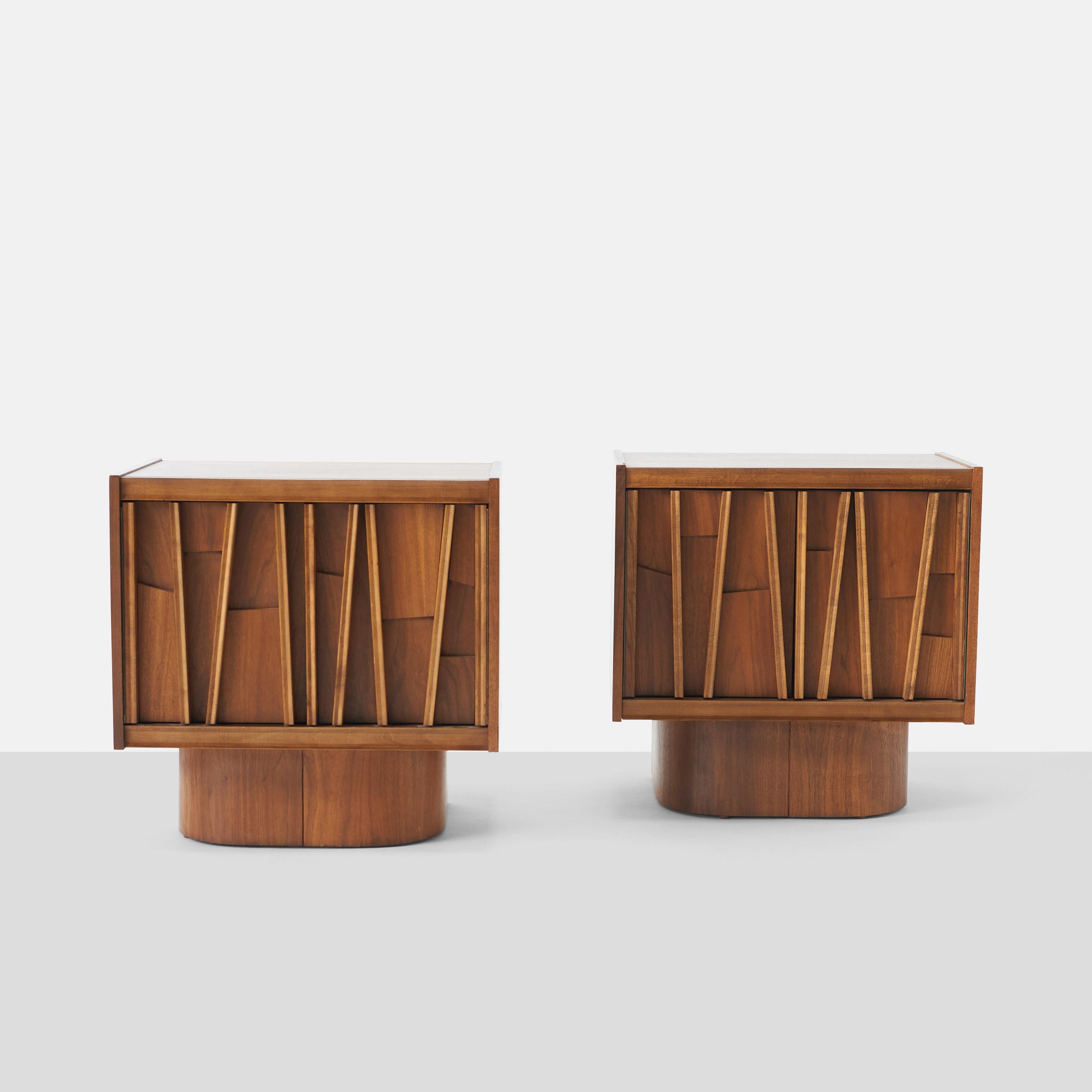 A pair of brutalist night stands or side tables of walnut. Swing out cabinet doors with shelving and pedestal base.

