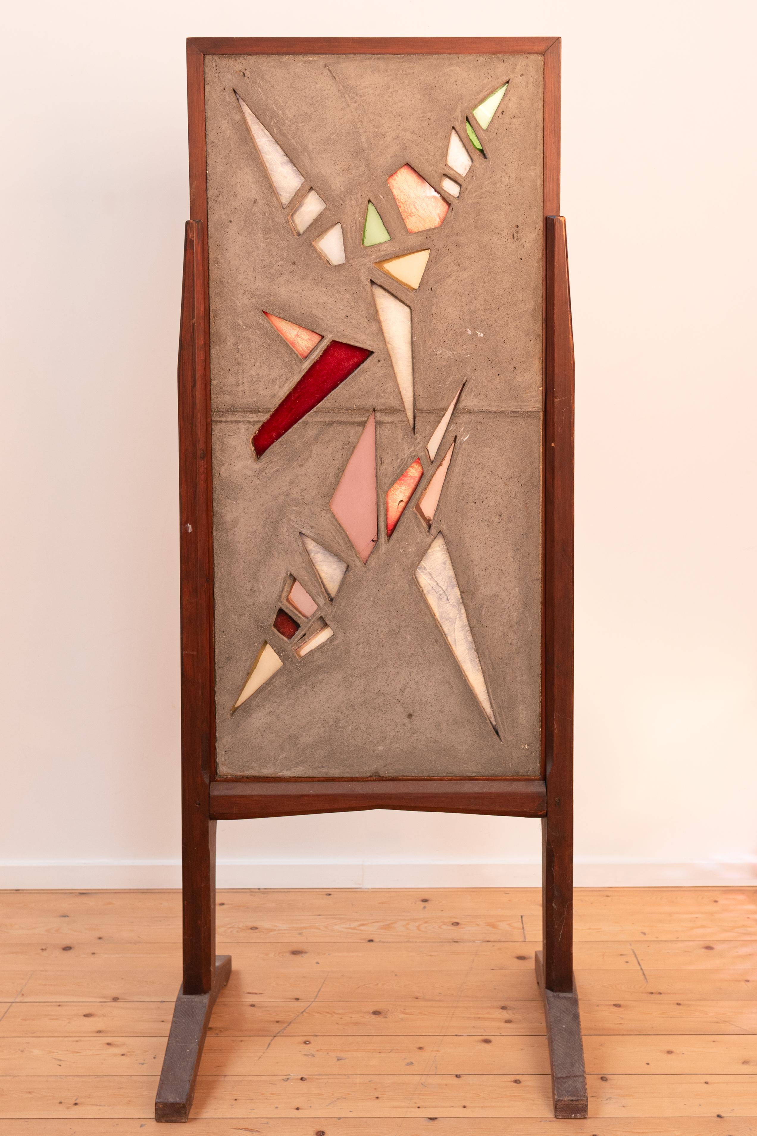 A Brutalist panel featuring geometrically cut colored glass set in concrete, all encased in a sturdy wooden frame.