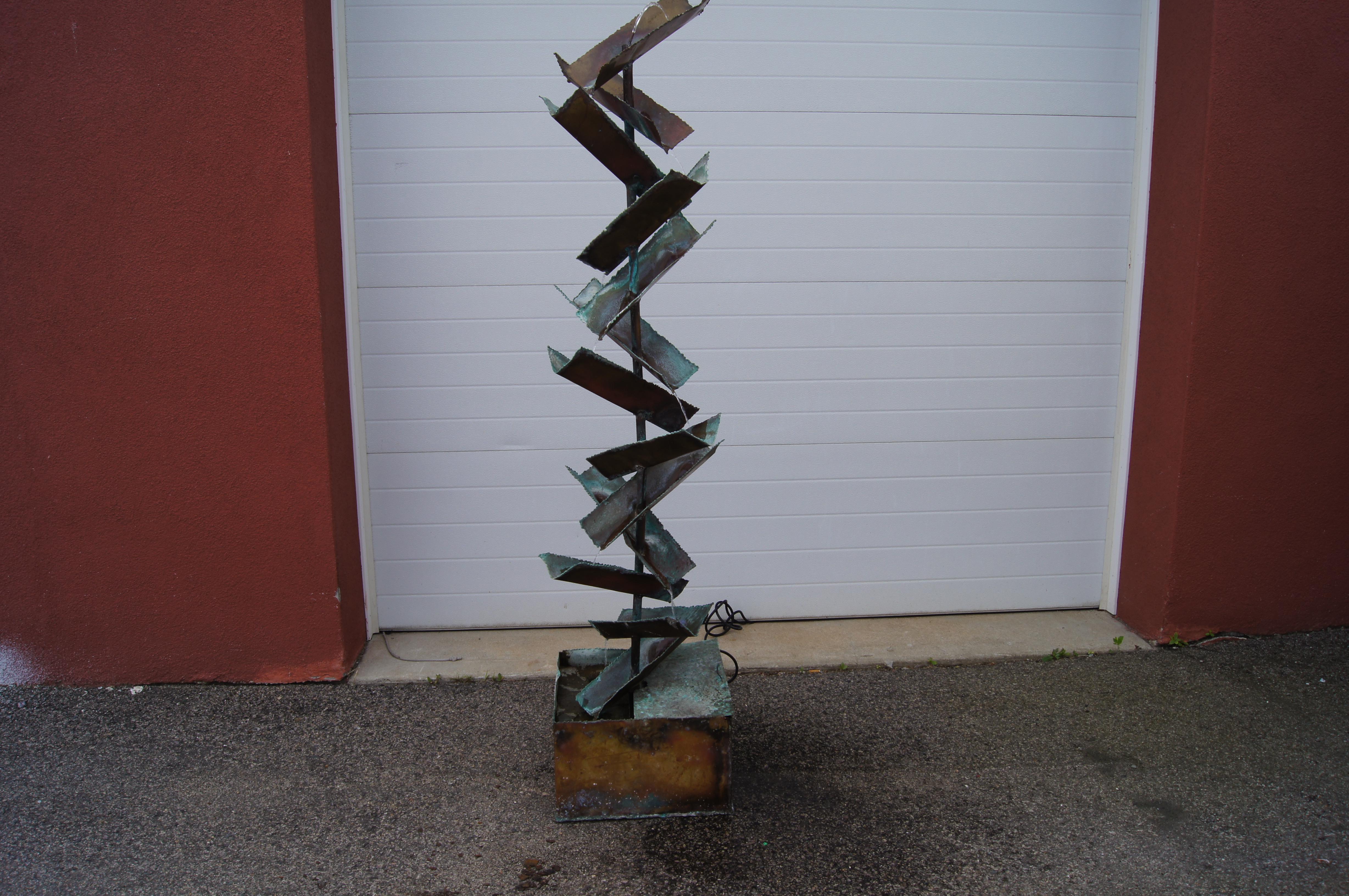 Silas Seandel designed this tall sculptural fountain of patinated copper. The water makes a lovely sound as it flows down the piece in two streams from tier to tier of folded channels. Signed on top channel.

The water pump has been replaced and