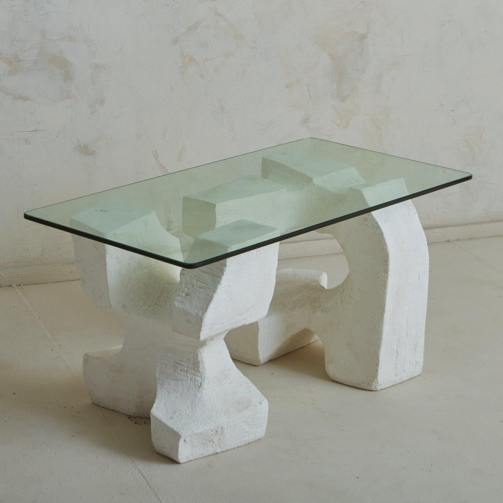 A vintage Brutalist French coffee table featuring a sculptural white plaster base with organic curves and a textured finish. The artful, asymmetric base is composed of two elements which support a rectangular glass tabletop with a beveled edge.
