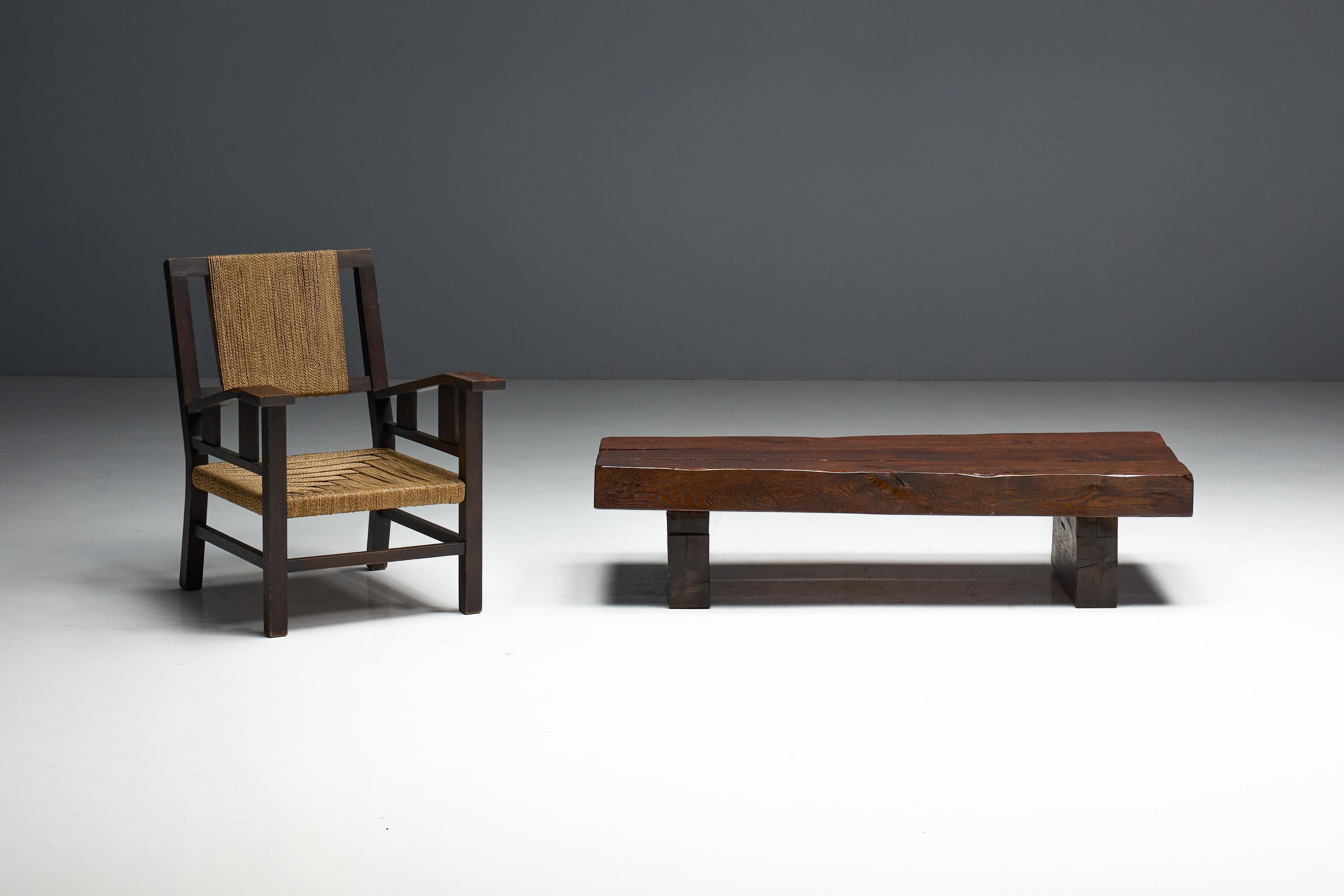 This brutalist coffee table is crafted from solid oak beams, showcasing the raw beauty of natural imperfections. Its substantial form, visible cracks, and rich patina highlight the organic texture of aged wood. The low profile and robust proportions